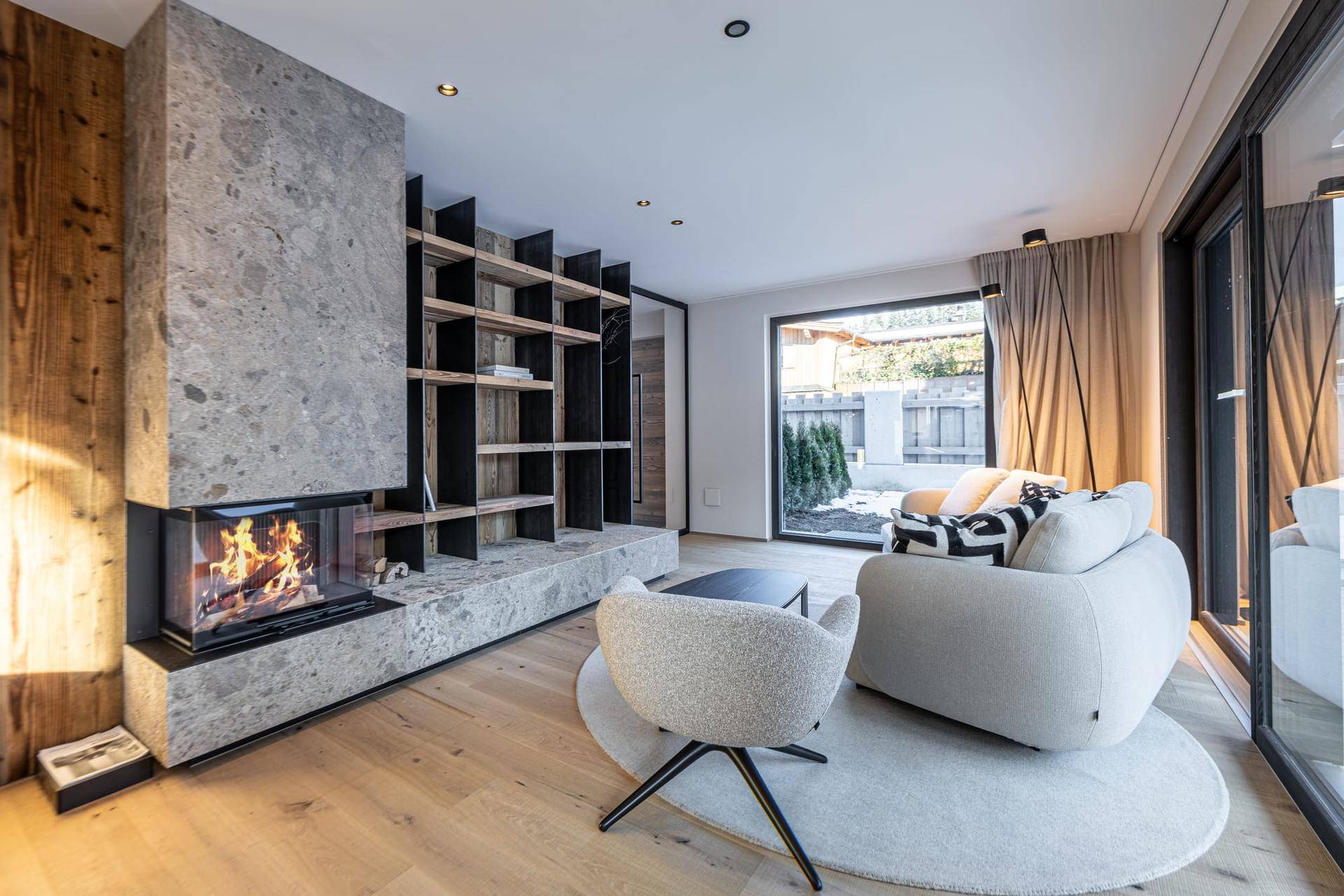 Gemütliches Wohnzimmer mit modernem Kamin, Holzboden und großen Fenstern zum Garten.