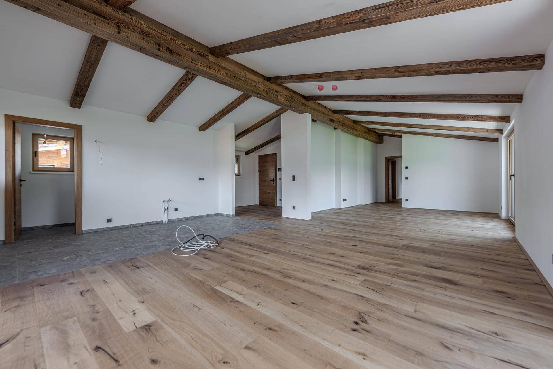 Geräumiger, unmöblierter Wohnbereich mit sichtbaren Holzbalken und neuem Holzboden, bereit für den Innenausbau.