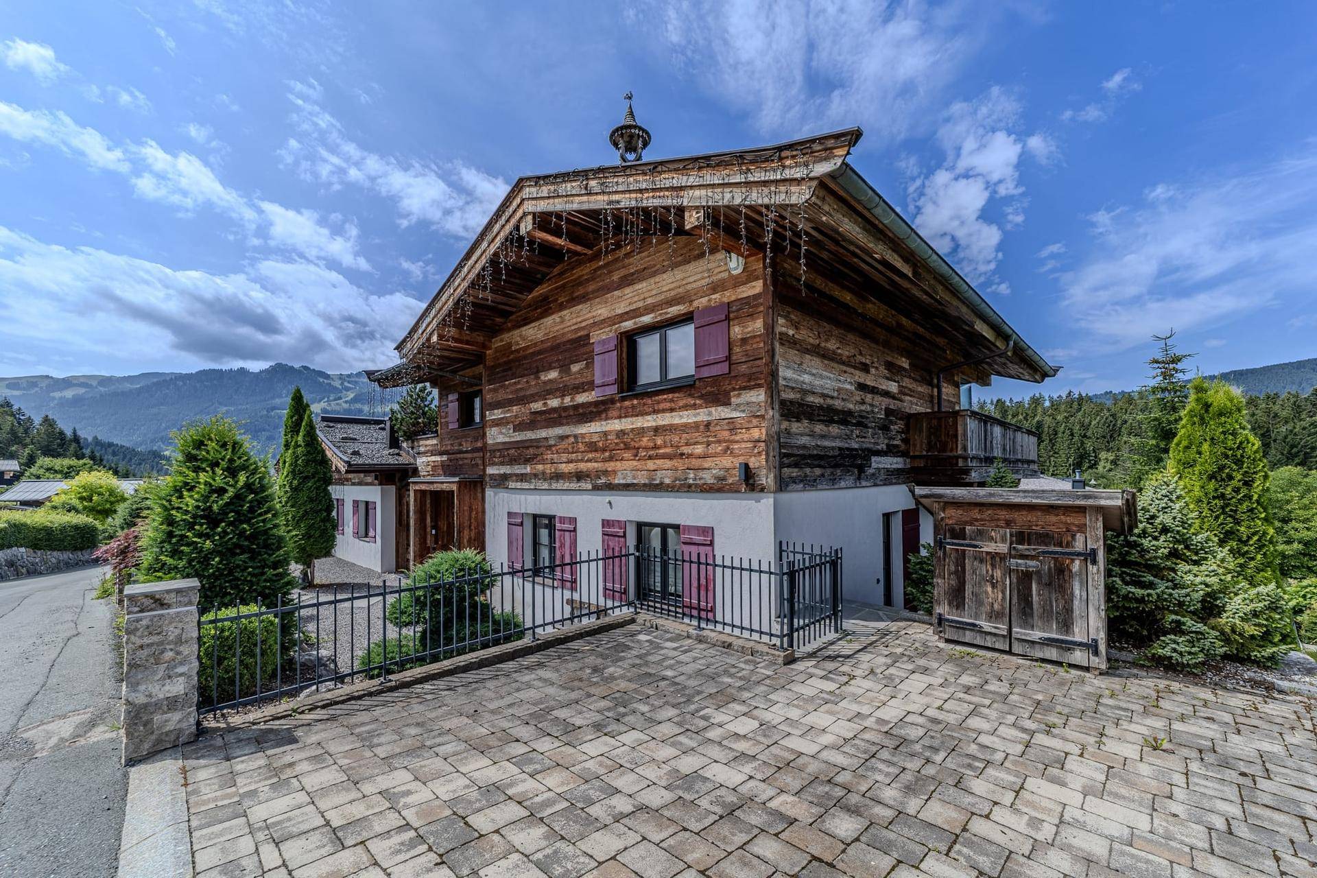 Traditionelles Holzchalet mit Satteldach, roten Fensterläden und gepflasterter Auffahrt in alpiner Umgebung.