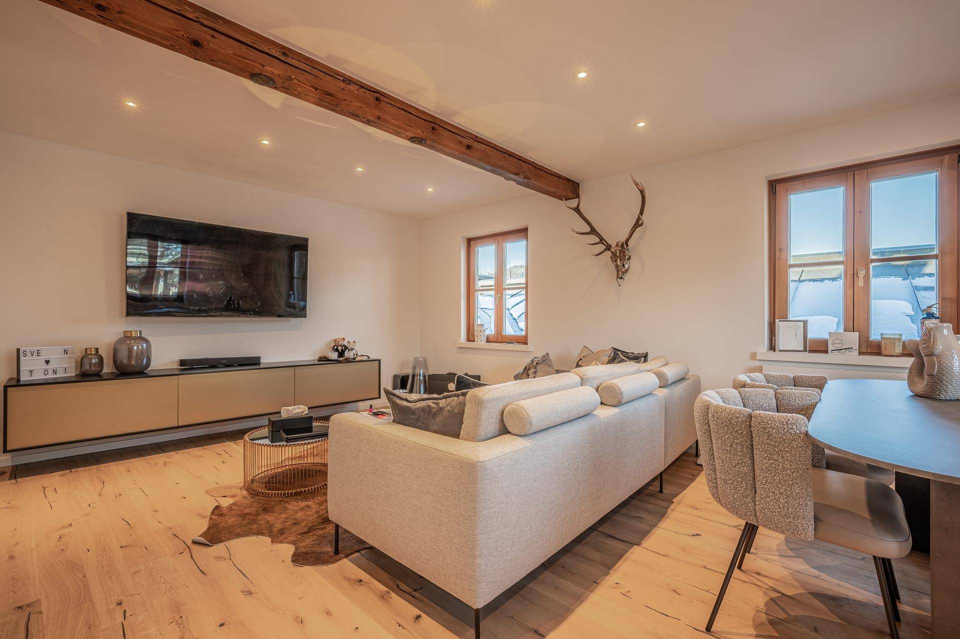 Helles Wohnzimmer mit Holzboden, modernem Sofa, Fernseher und sichtbaren Deckenbalken.