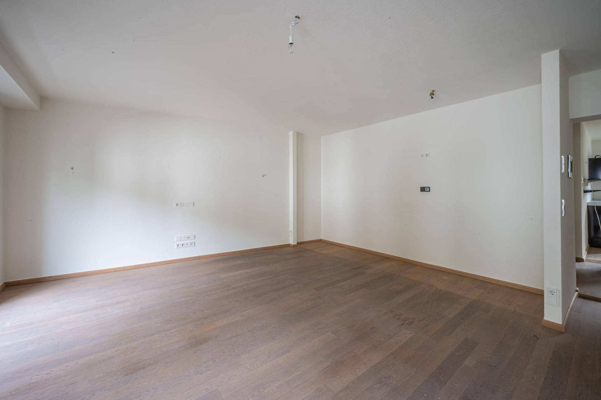 Heller, leerer Raum mit dunklem Holzboden und sauberen weißen Wänden, bereit zur individuellen Gestaltung.