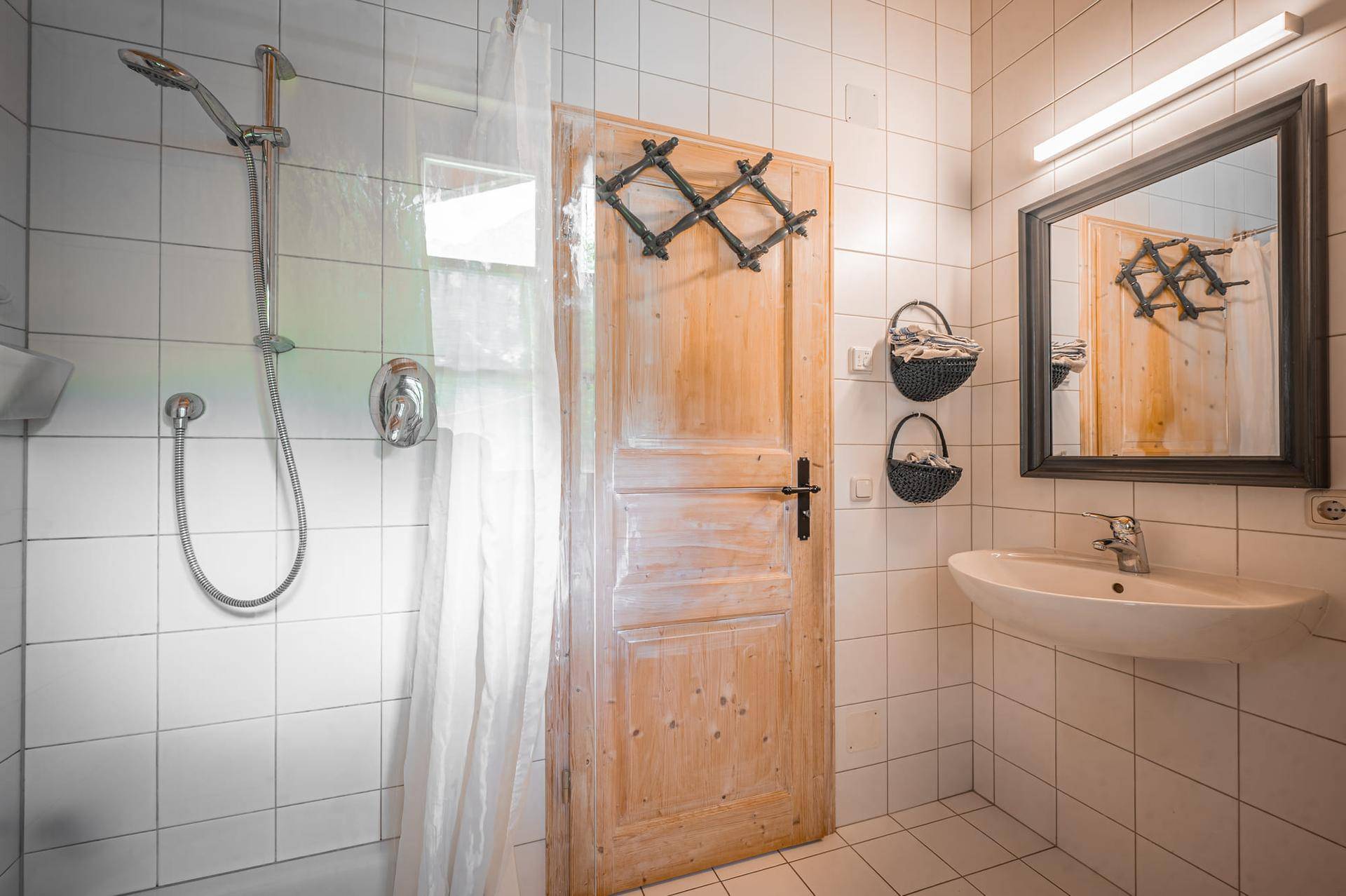 Funktionales Badezimmer mit weißen Fliesen, Dusche und Waschbecken.
