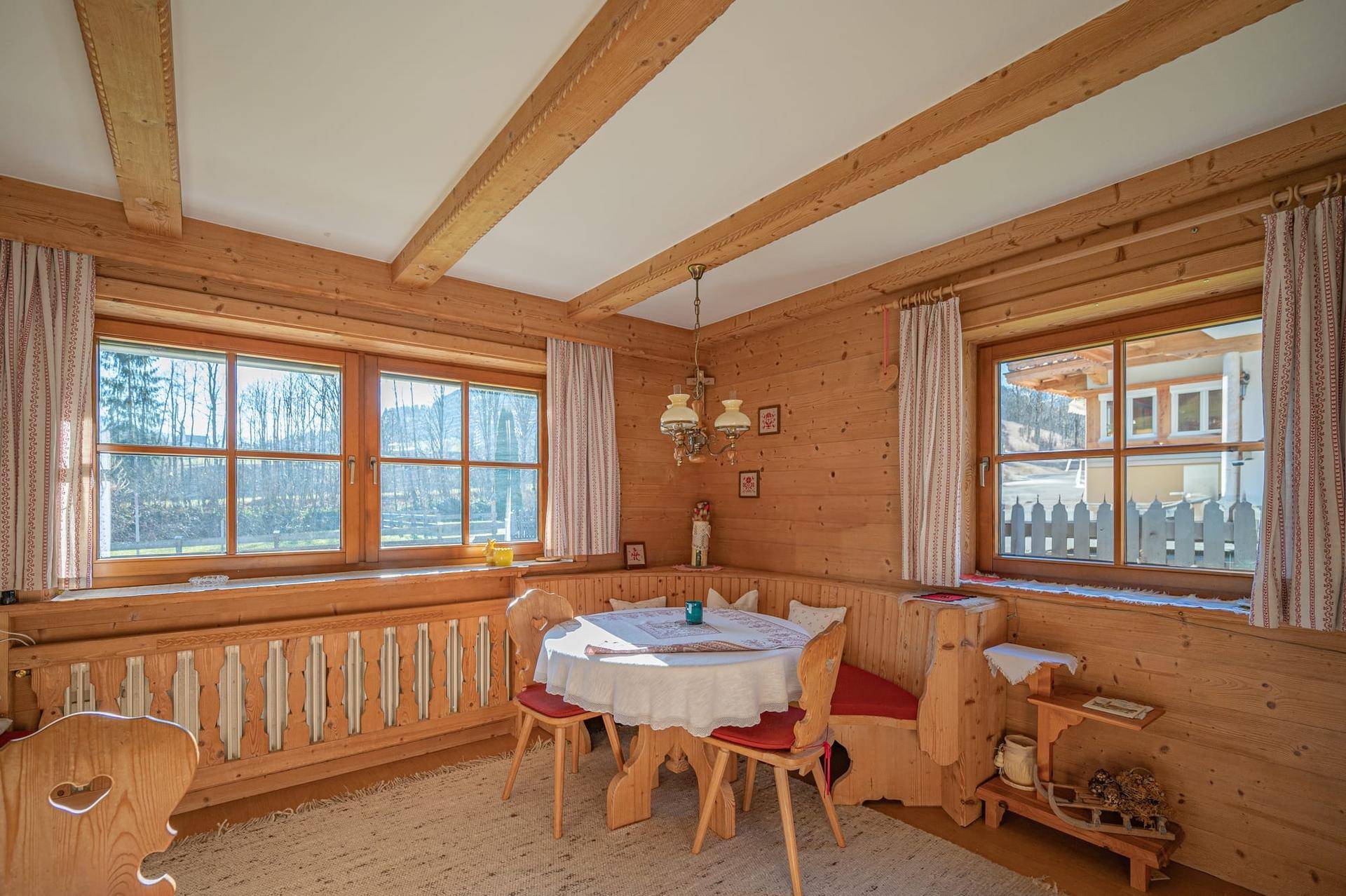 Heller Essbereich im Landhausstil mit Holzbalken, Eckbank und Blick ins Grüne.
