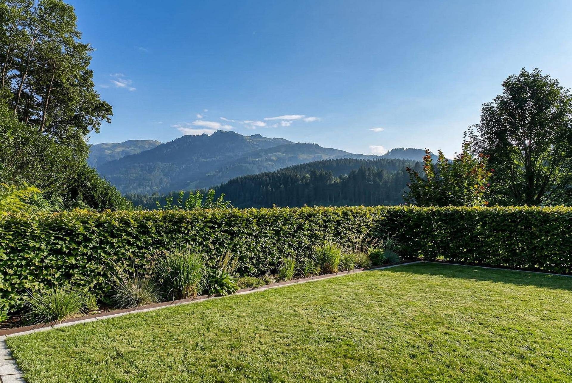 Gepflegter Gartenbereich mit Hecke und weitem Blick auf die umliegende Berglandschaft.
