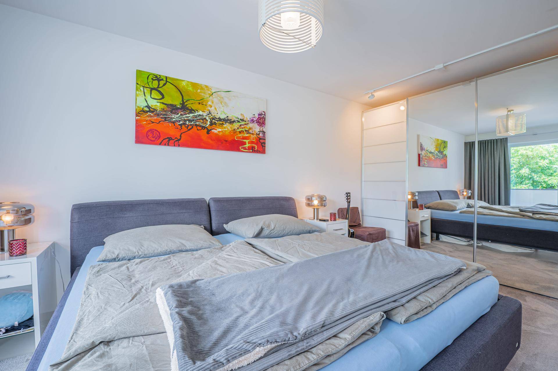Geräumiges Schlafzimmer mit Doppelbett, farbenfrohem Kunstwerk und großem Spiegelschrank.