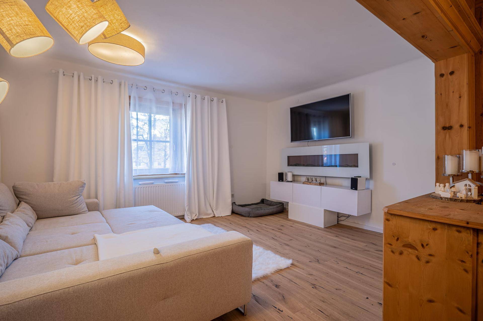 Helles Wohnzimmer mit bequemem Ecksofa, Fernseher an der Wand und Holzboden.