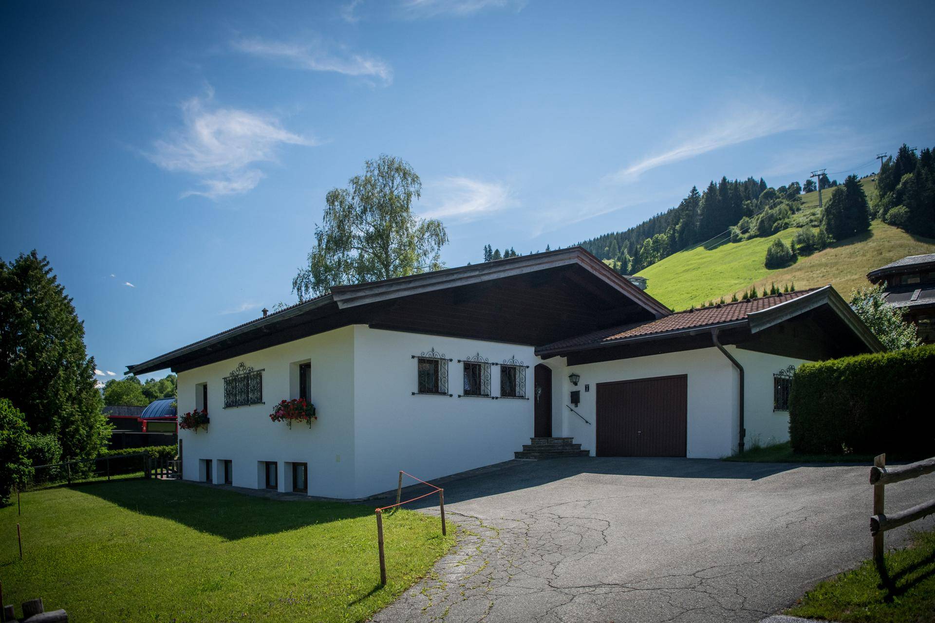 Einfamilienhaus mit weißer Fassade und Satteldach in alpiner Umgebung, umgeben von Grünflächen.