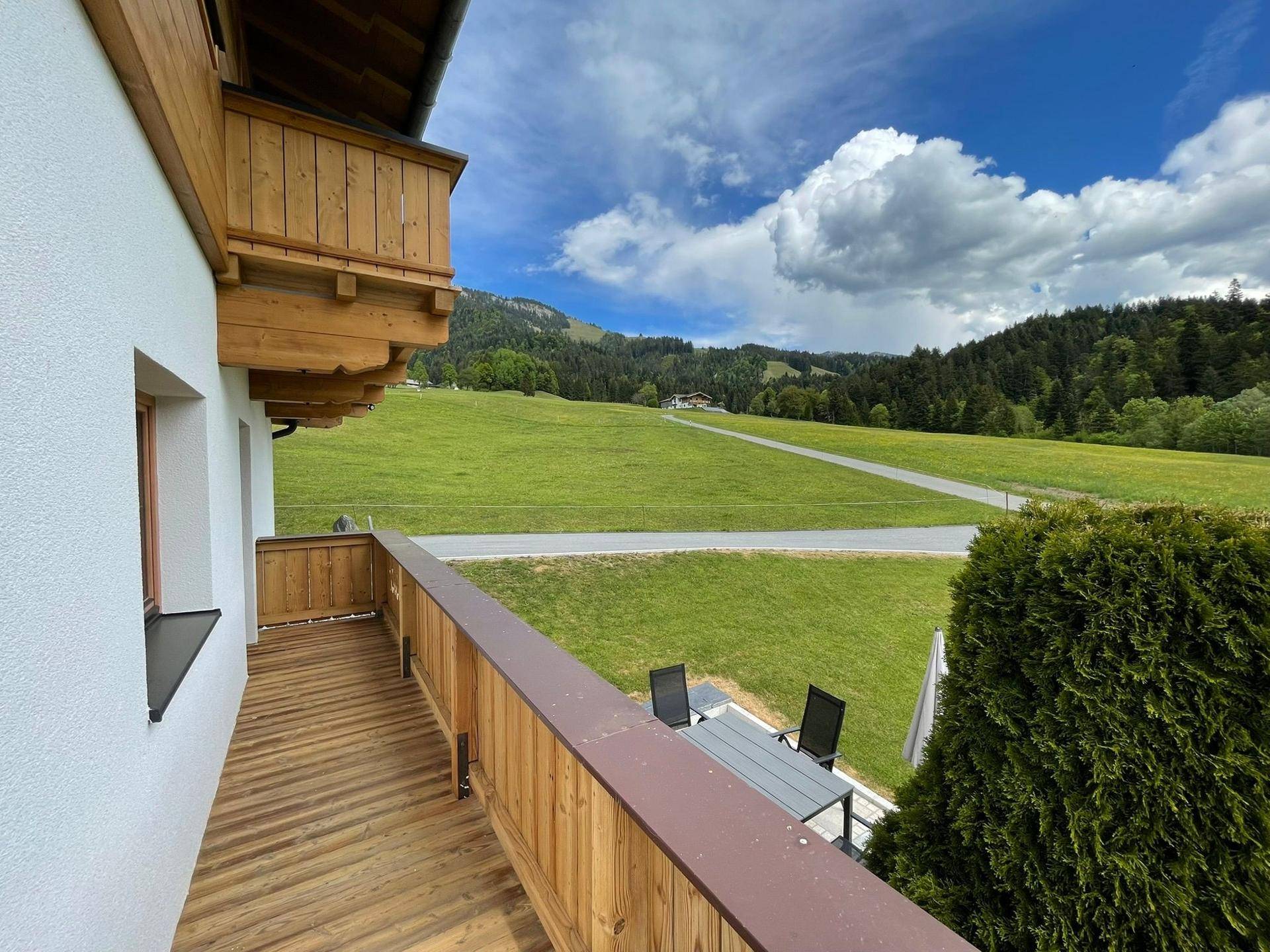 Geräumiger Holzbalkon mit Sitzgelegenheiten und weitem Blick auf die umliegende Berglandschaft.