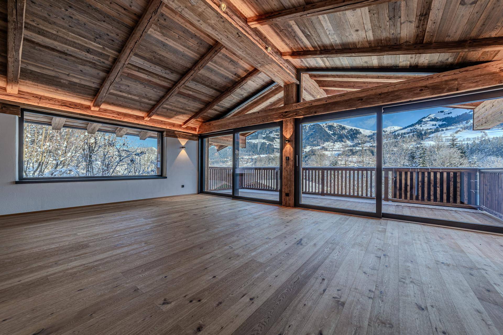 Geräumiger Wohnbereich mit Holzboden, hohen Decken und Panoramafenstern mit Bergblick.