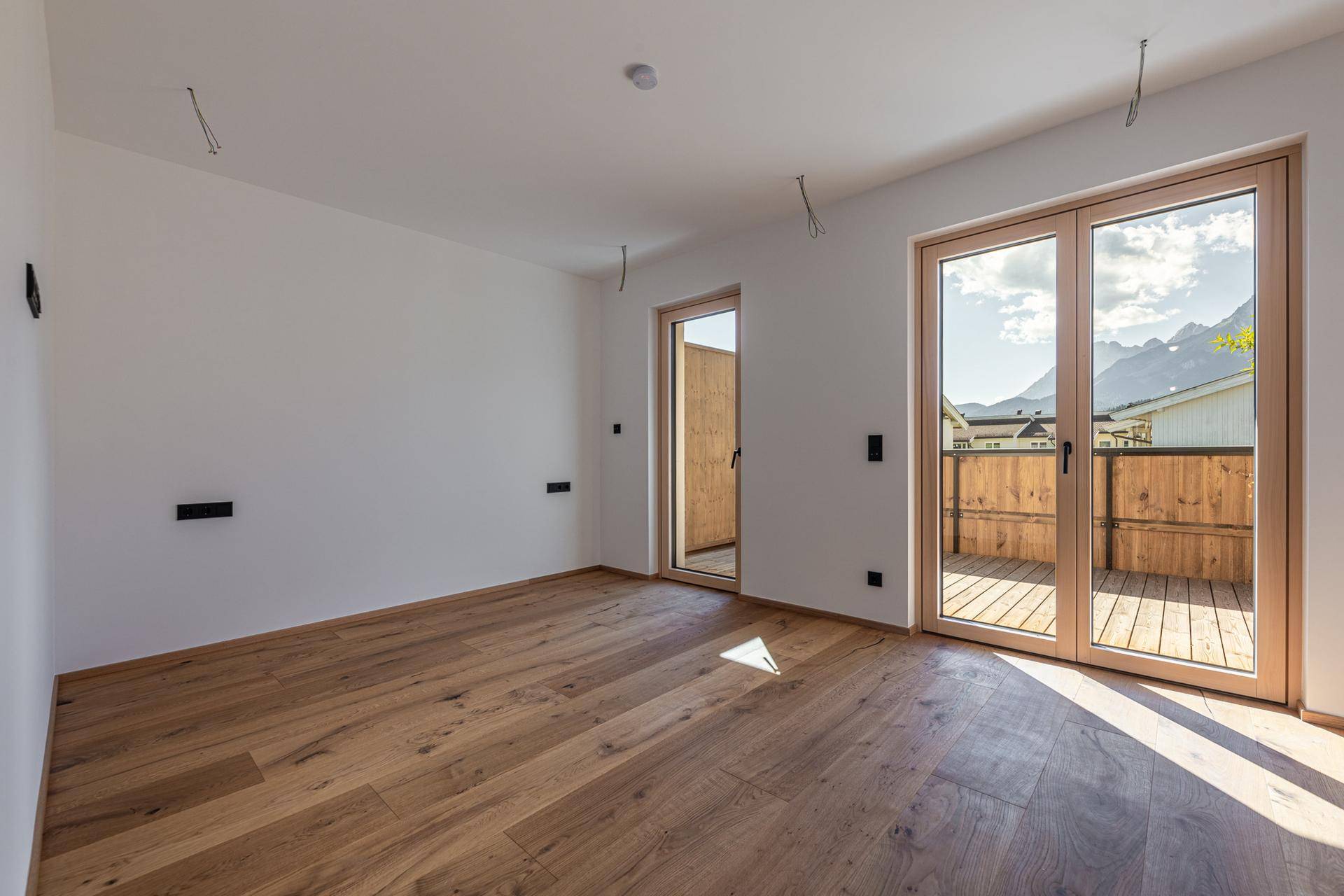 Schlafzimmer mit edlem Holzboden, großen Fenstern und direktem Zugang zur Terrasse.