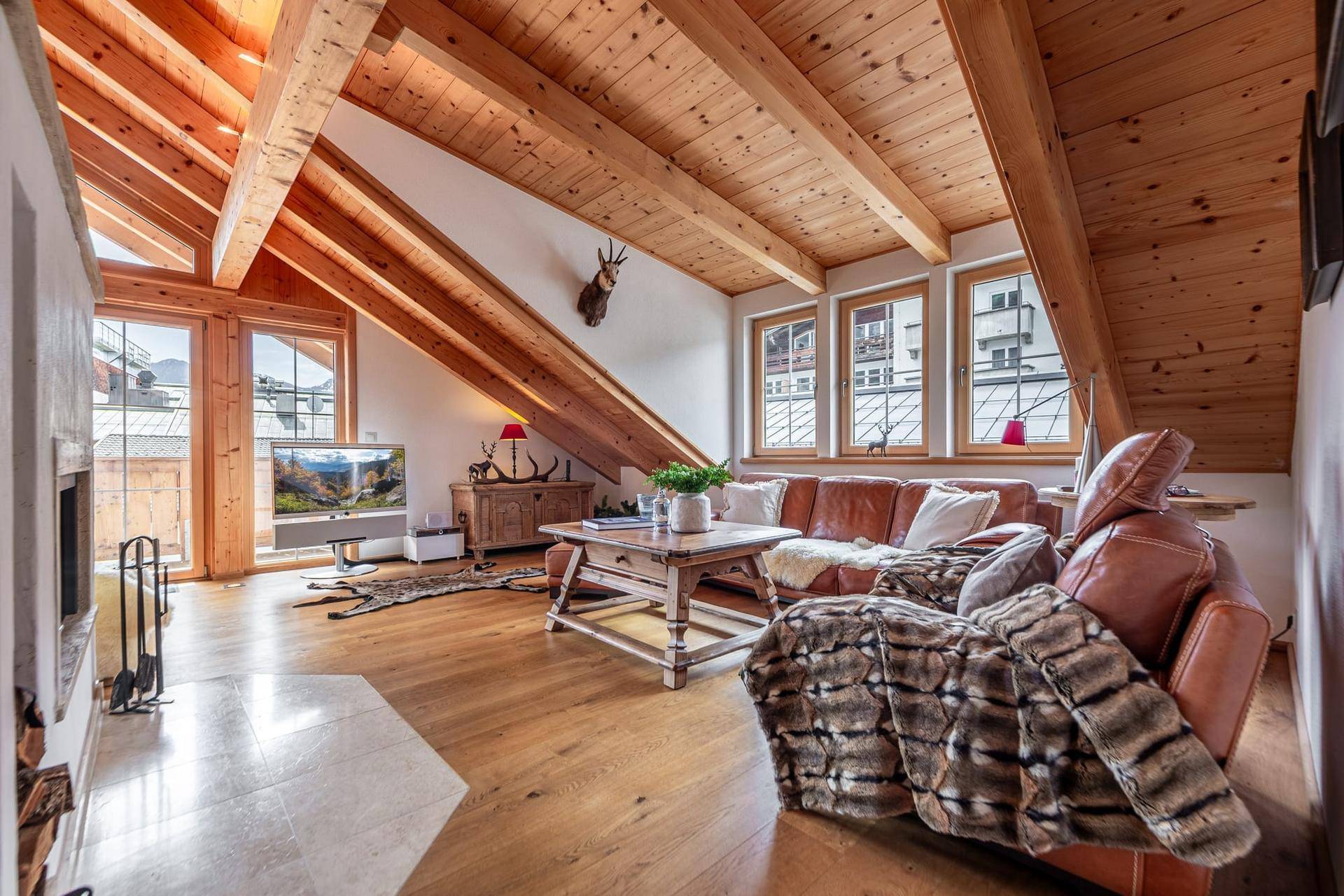 Helles Wohnzimmer mit Holzbalkendecke, Kamin und weitem Blick auf die umliegende Berglandschaft.