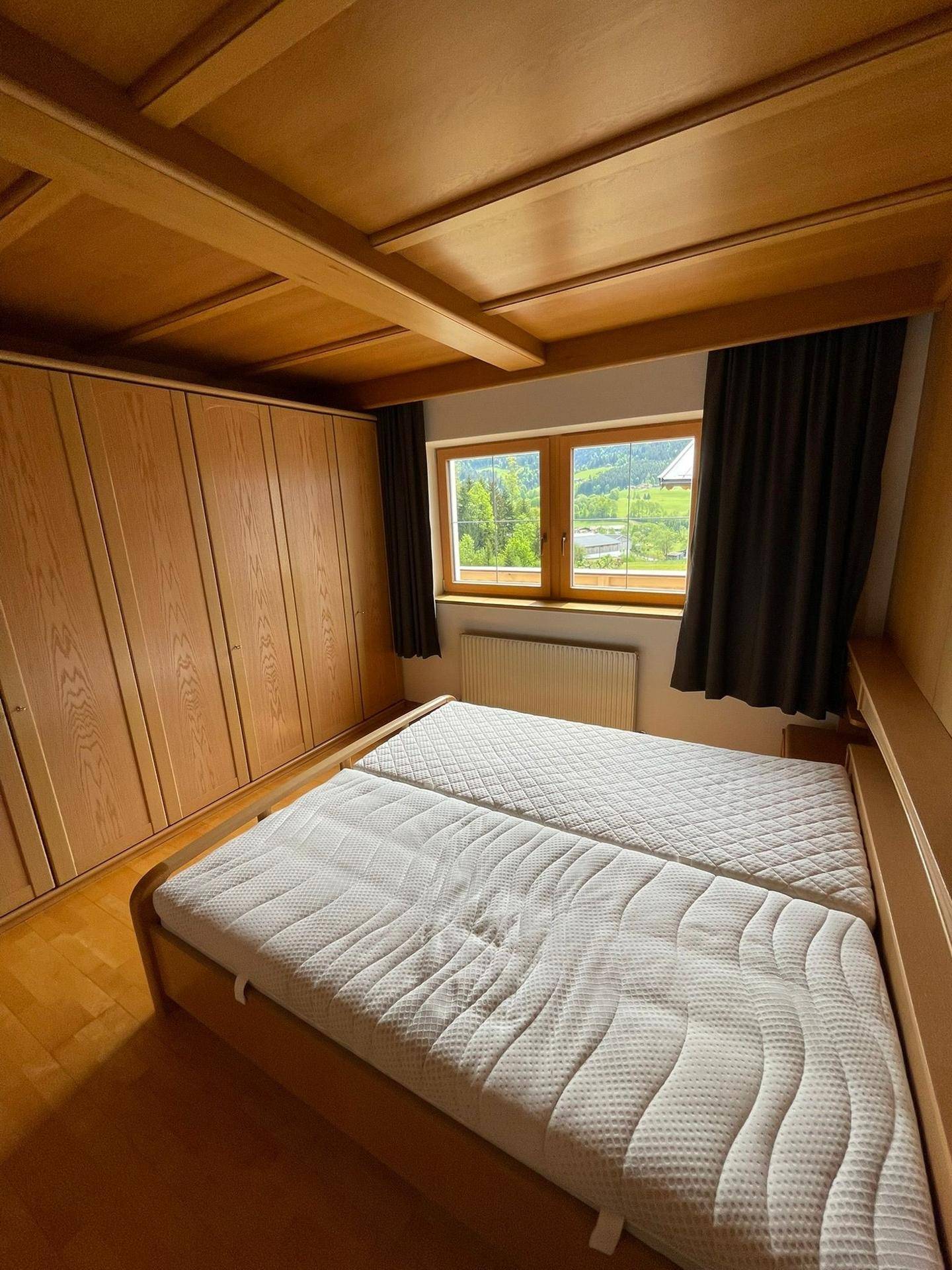 Gemütliches Schlafzimmer mit zwei Einzelbetten, Holzschränken und Blick auf die grüne Landschaft.