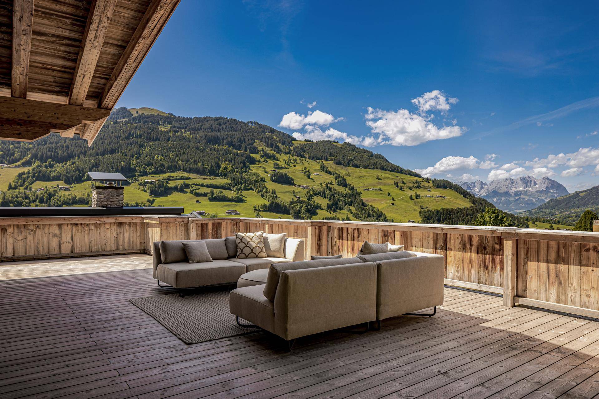 Großzügige Holzterrasse mit bequemen Loungemöbeln und spektakulärem Blick auf die grüne Berglandschaft.