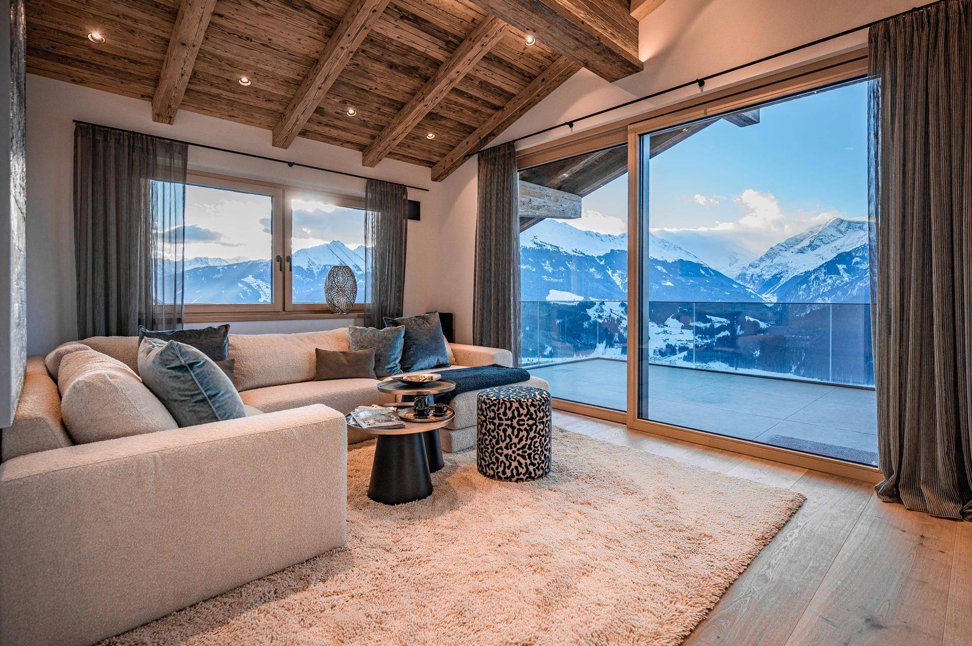 Gemütliches Wohnzimmer mit großem Sofa, Holzbalkendecke und beeindruckendem Bergblick.