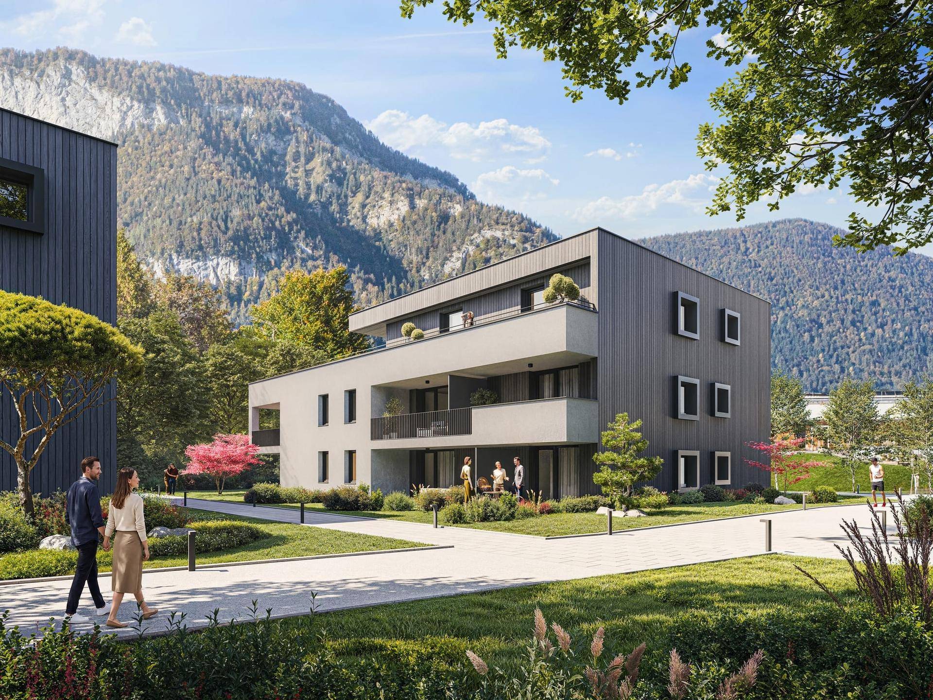 Moderne Wohngebäude in einer grünen Umgebung mit Bergblick unter blauem Himmel.