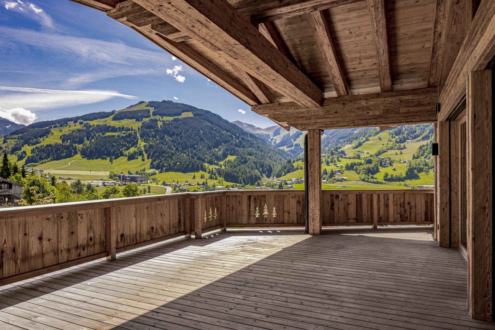 Großer Holzbalkon mit weitem Blick auf die grüne Berglandschaft und das Tal darunter.