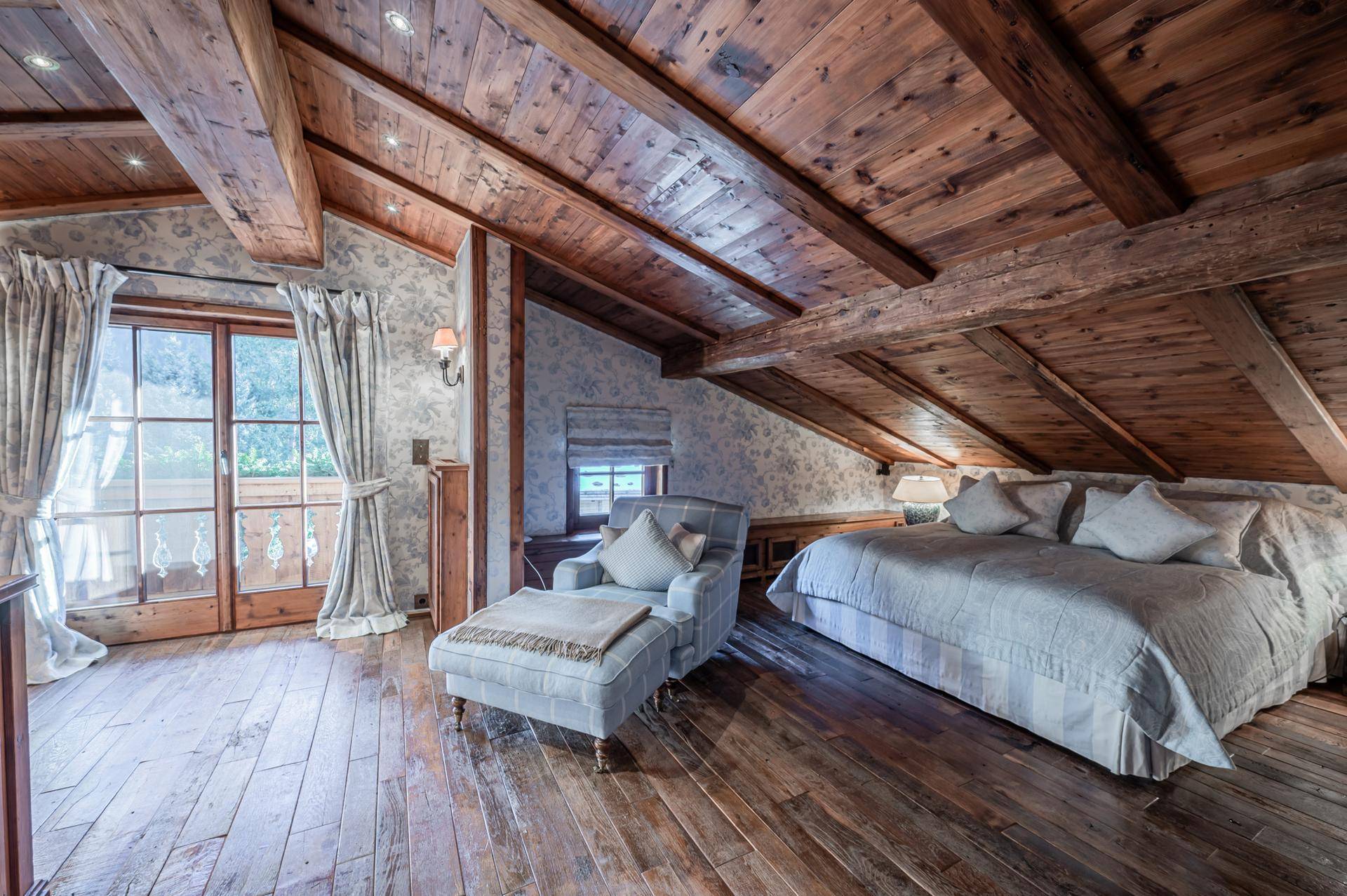 Helles Schlafzimmer im Dachgeschoss mit Holzbalken, schrägen Decken und Balkonzugang.