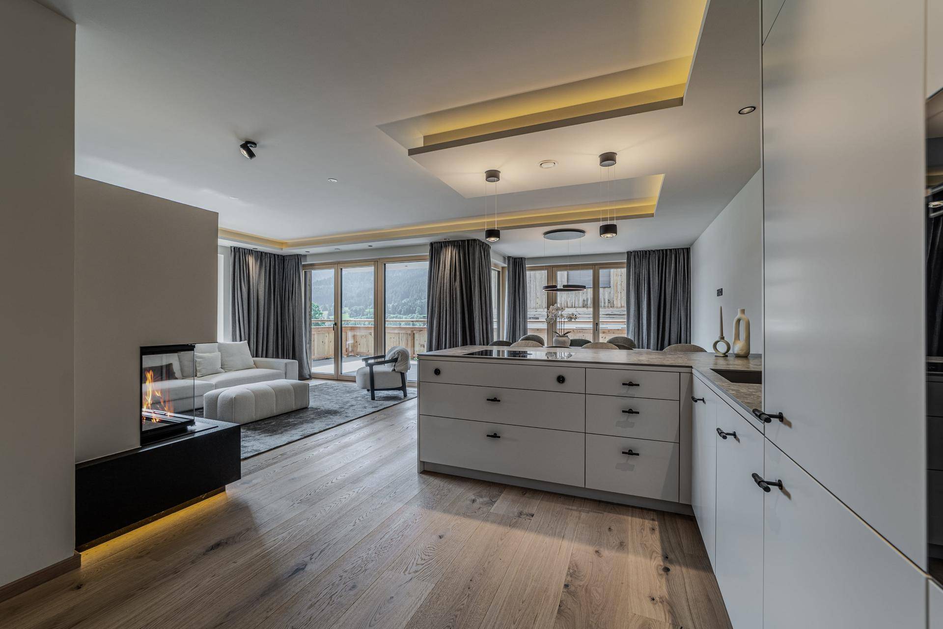 Moderner Wohnbereich mit Kamin, offener Küche und Zugang zu einem Balkon mit Bergblick.