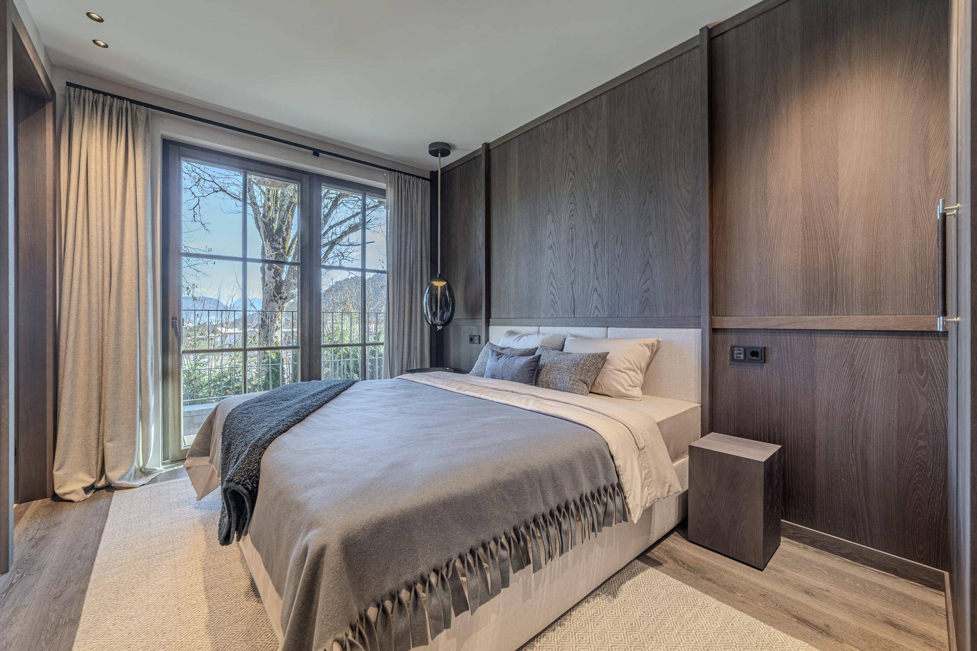 Elegantes Schlafzimmer mit dunkler Holzvertäfelung, großem Fenster und Blick ins Grüne.
