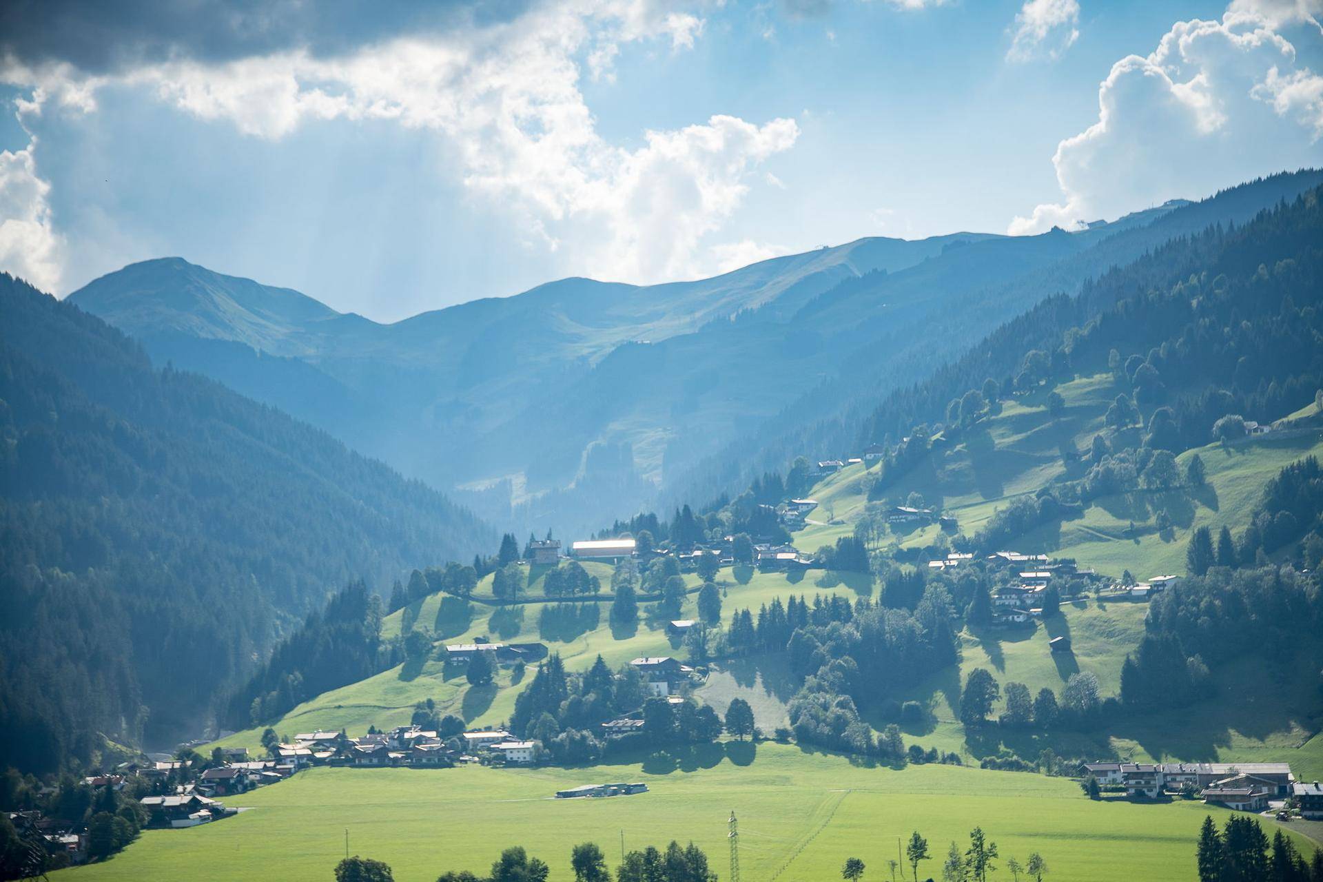 Weitläufiges Tal mit kleinen Dörfern, grünen Wiesen und bewaldeten Berghängen unter blauem Himmel.