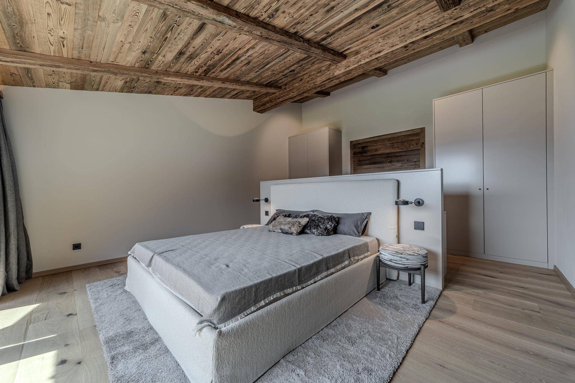 Helles Schlafzimmer mit Holzbalkendecke, Parkettboden und einem großen Bett mit integriertem Kopfteil.