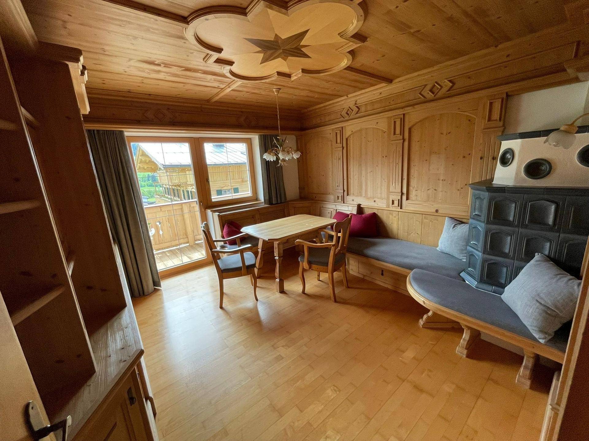 Gemütlicher Wohn-Essbereich im alpinen Stil mit Holztäfelung, Kachelofen und Zugang zum Balkon.