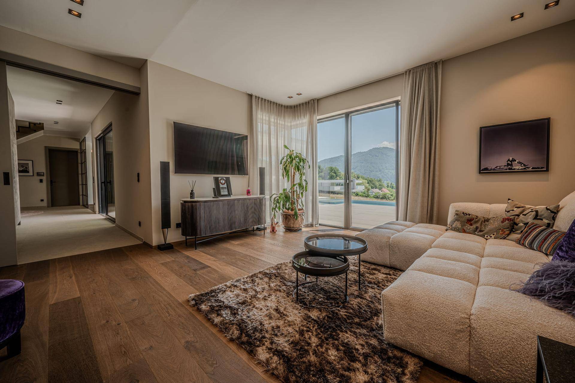 Helles Wohnzimmer mit Holzboden, großem Sofa und Panoramablick auf die umliegenden Berge durch bodentiefe Fenster.