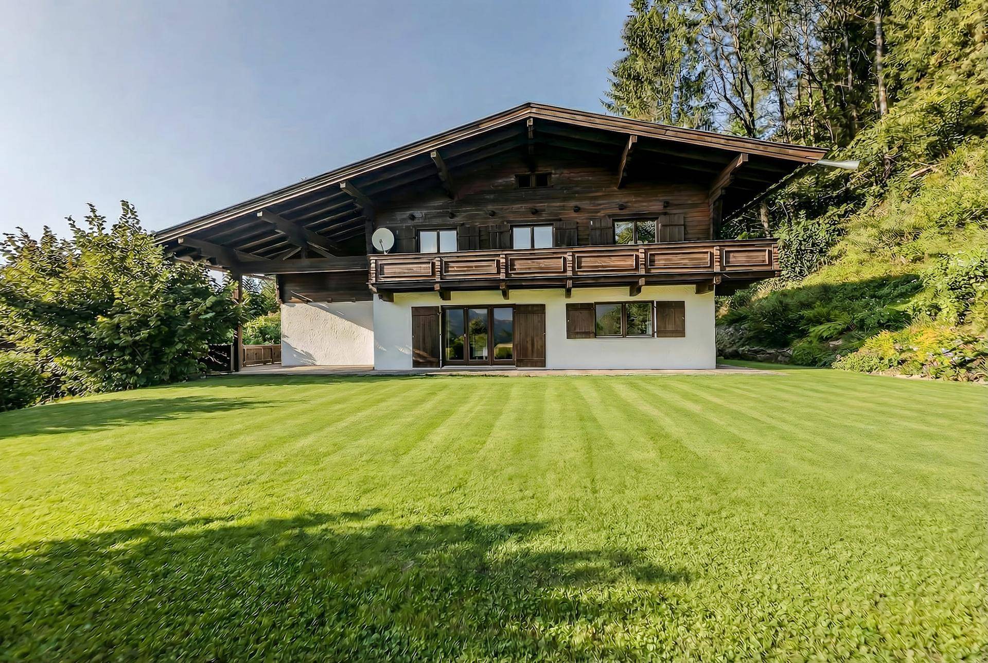 Traditionelles Holzhaus im Chalet-Stil mit großem Rasen und Balkon in alpiner Umgebung.