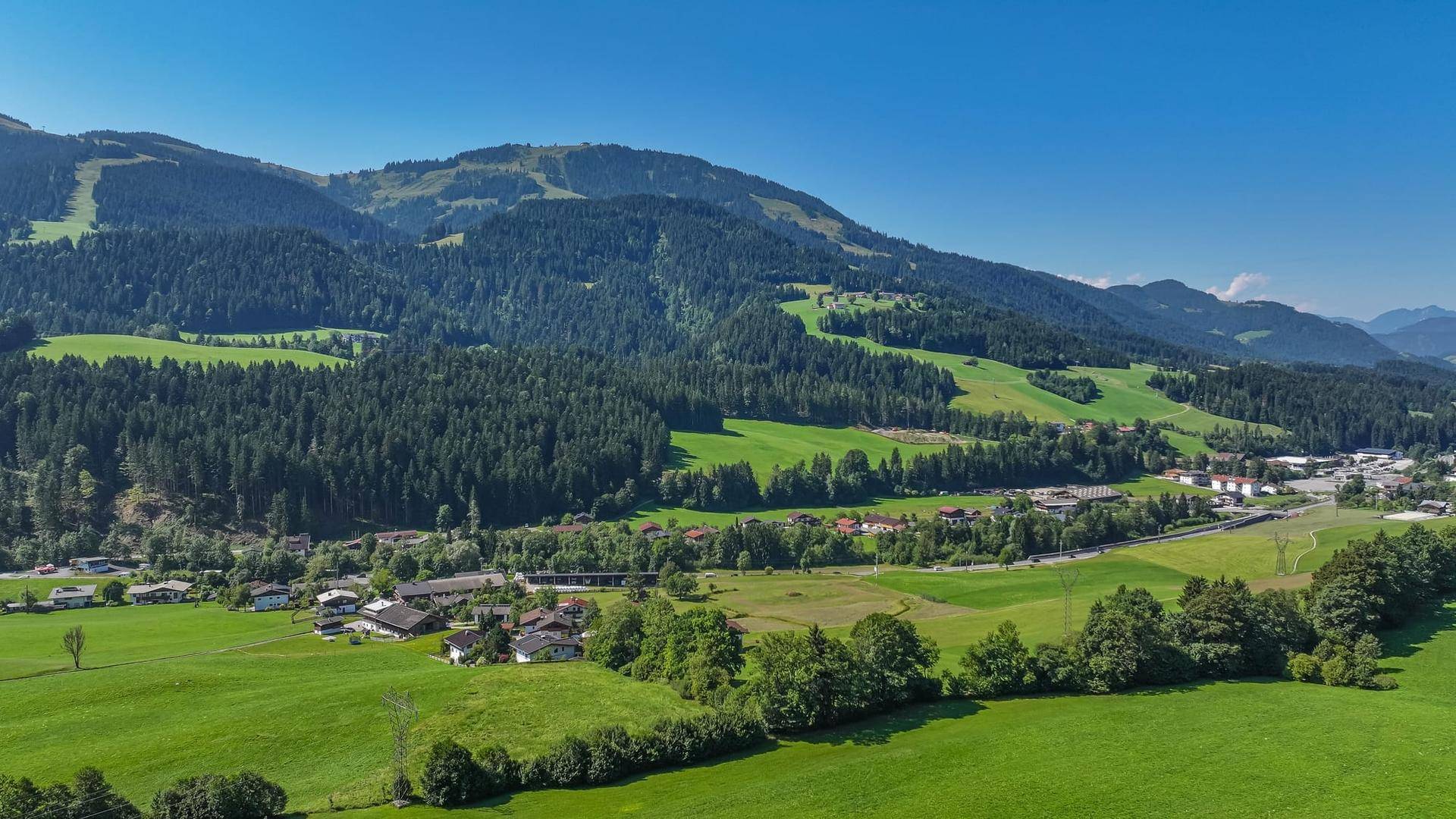 Panoramablick über ein grünes Tal mit einem Dorf, umgeben von Wäldern und Bergen.