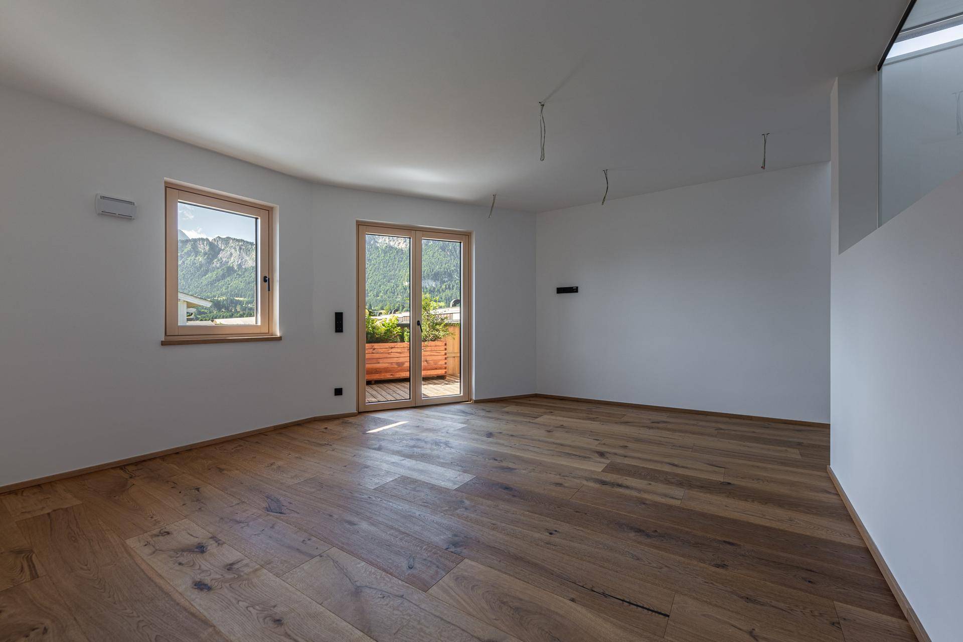 Geräumiger, heller Wohnbereich mit hochwertigem Holzboden und Fenstern mit Bergblick.