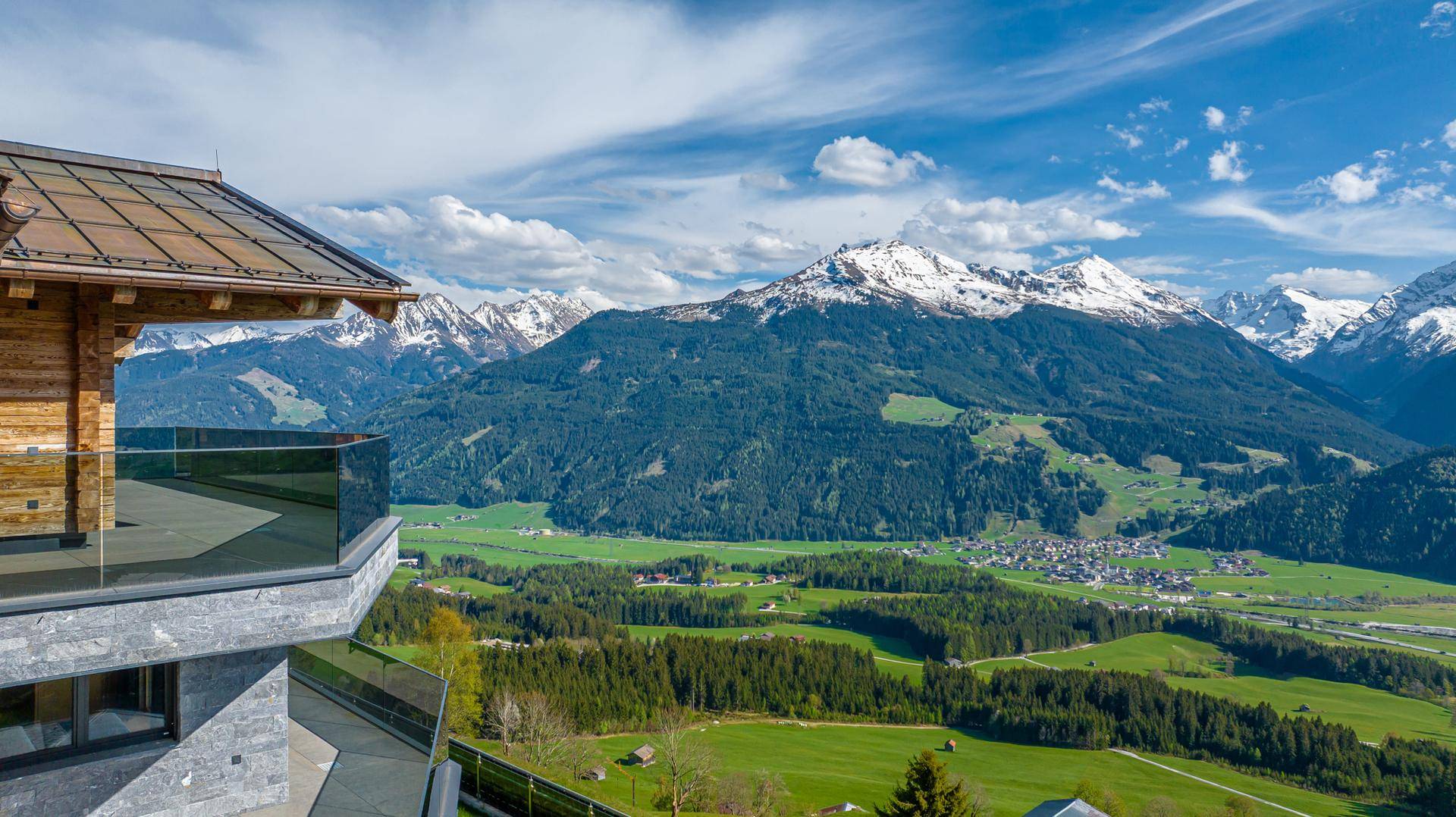 Moderner Balkon mit Glasgeländer und atemberaubendem Blick auf die schneebedeckten Berge und grüne Täler.