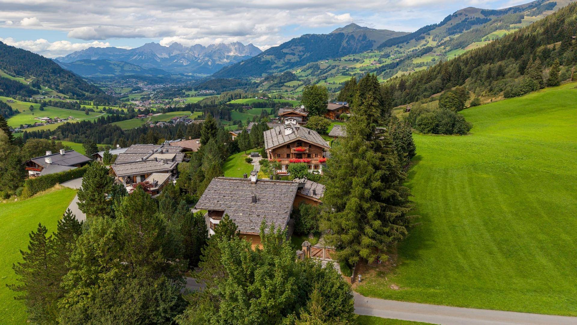 Weitläufige Luftaufnahme einer Chalet-Siedlung in einem grünen Tal mit majestätischem Bergblick.