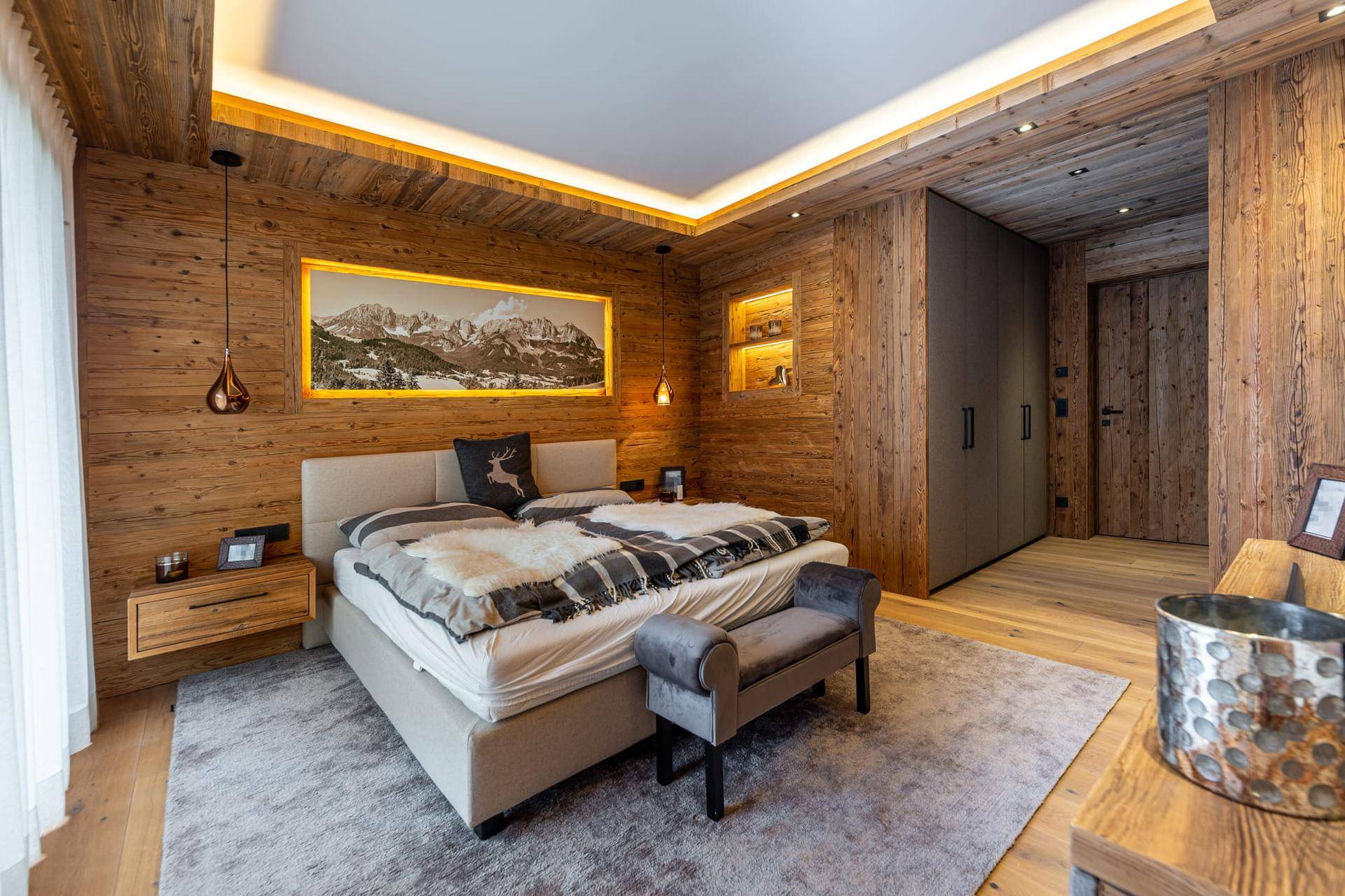 Gemütliches Schlafzimmer im alpinen Stil mit Holzwänden, Doppelbett und indirekter Beleuchtung.