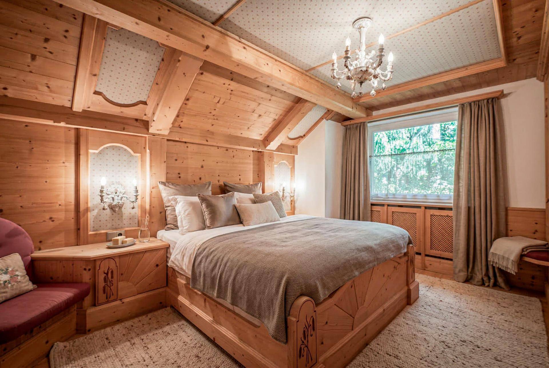 Gemütliches Schlafzimmer im alpinen Stil mit Holzbalken, Doppelbett und Kronleuchter.