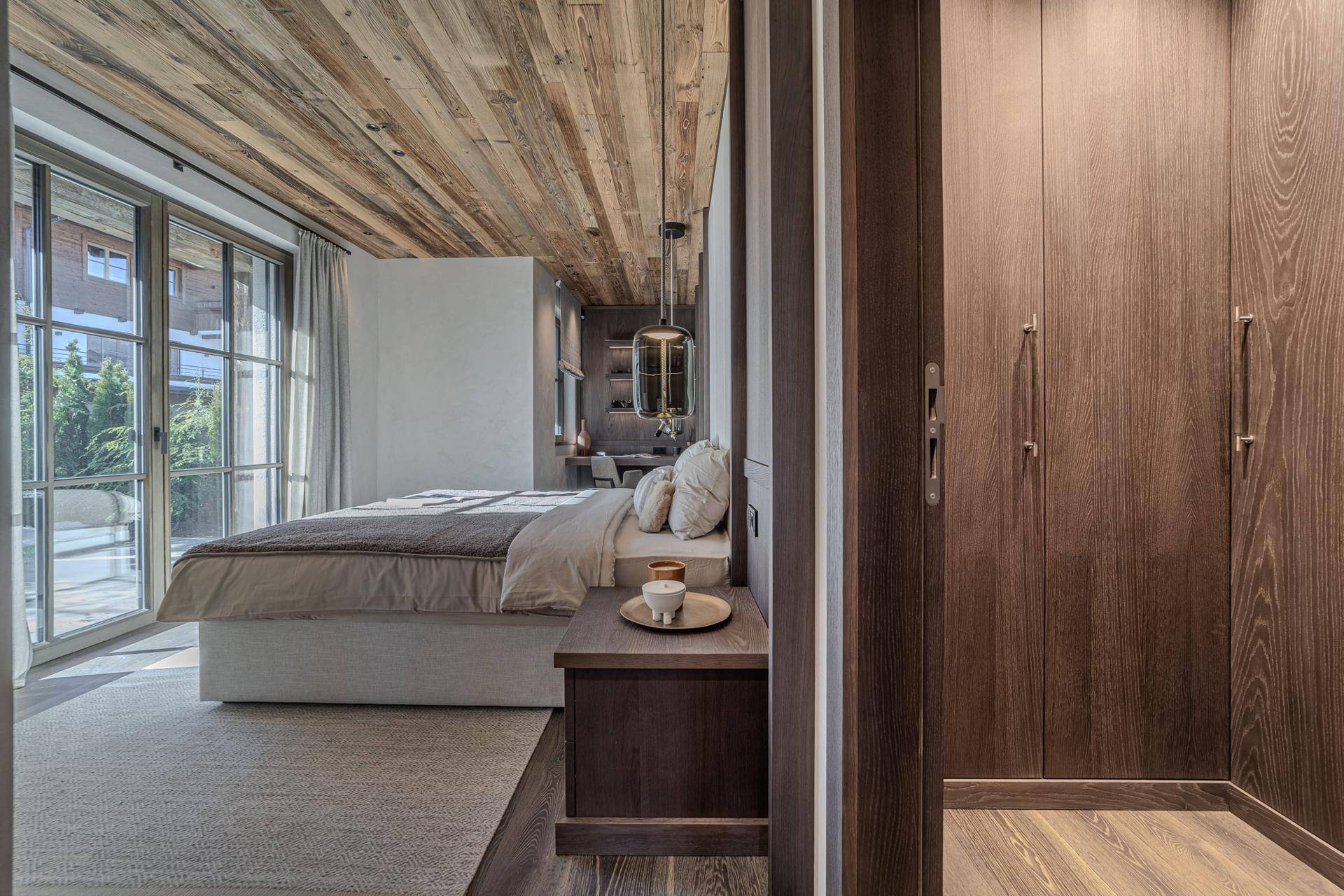 Helles Schlafzimmer mit integrierten Kleiderschränken, Holzboden und Zugang zur Terrasse.