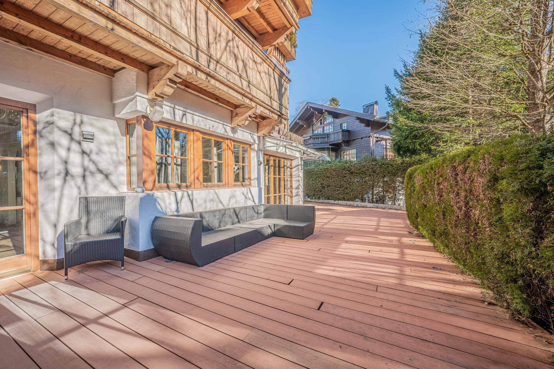 Große Holzterrasse mit modernen Gartenmöbeln und Hecke im Außenbereich.