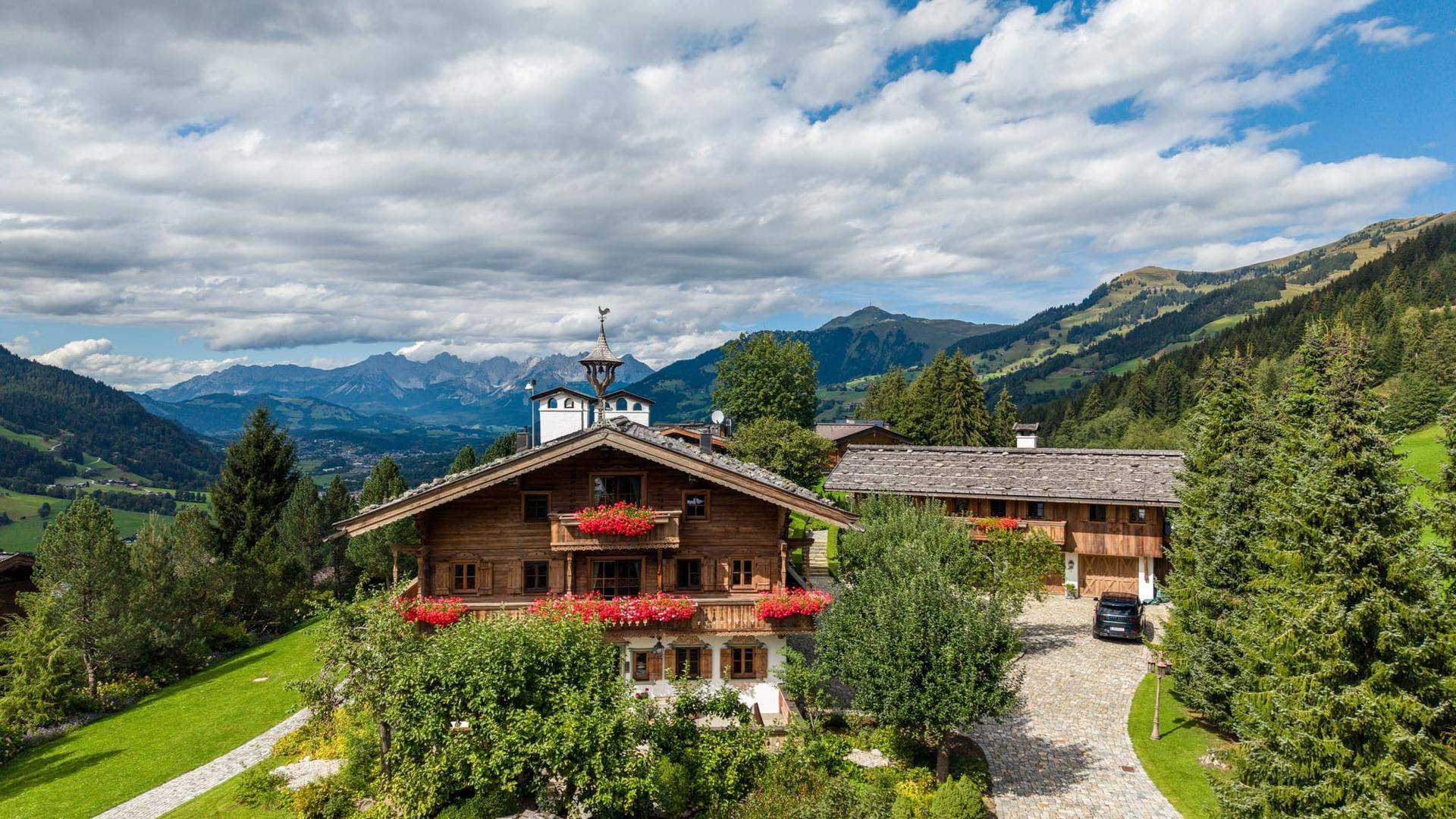 Traditionelles Holzchalet mit Blumenkästen und Bergblick unter bewölktem Himmel.
