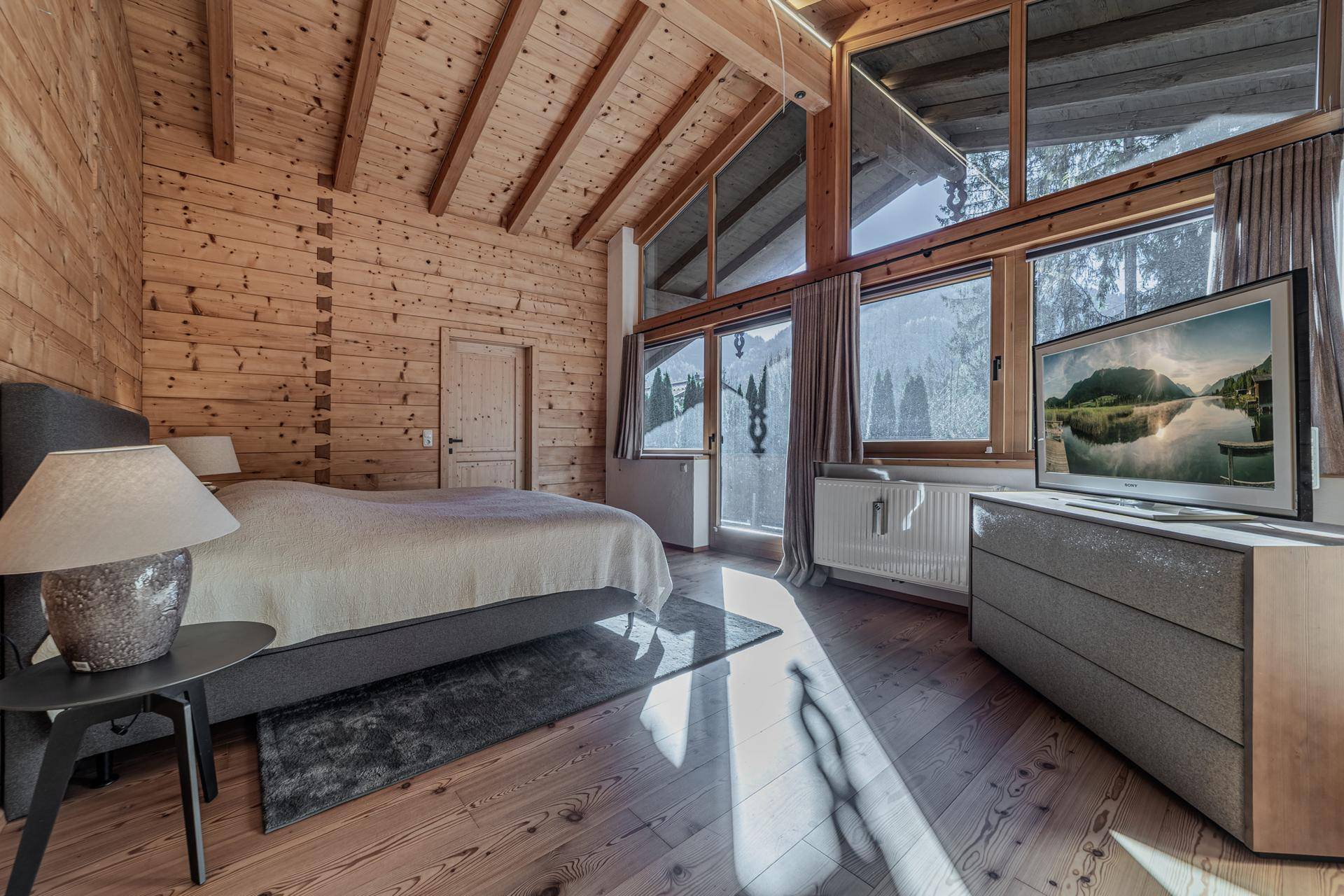Helles Schlafzimmer mit Holzwänden, hohen Decken und großen Fenstern mit Bergblick.