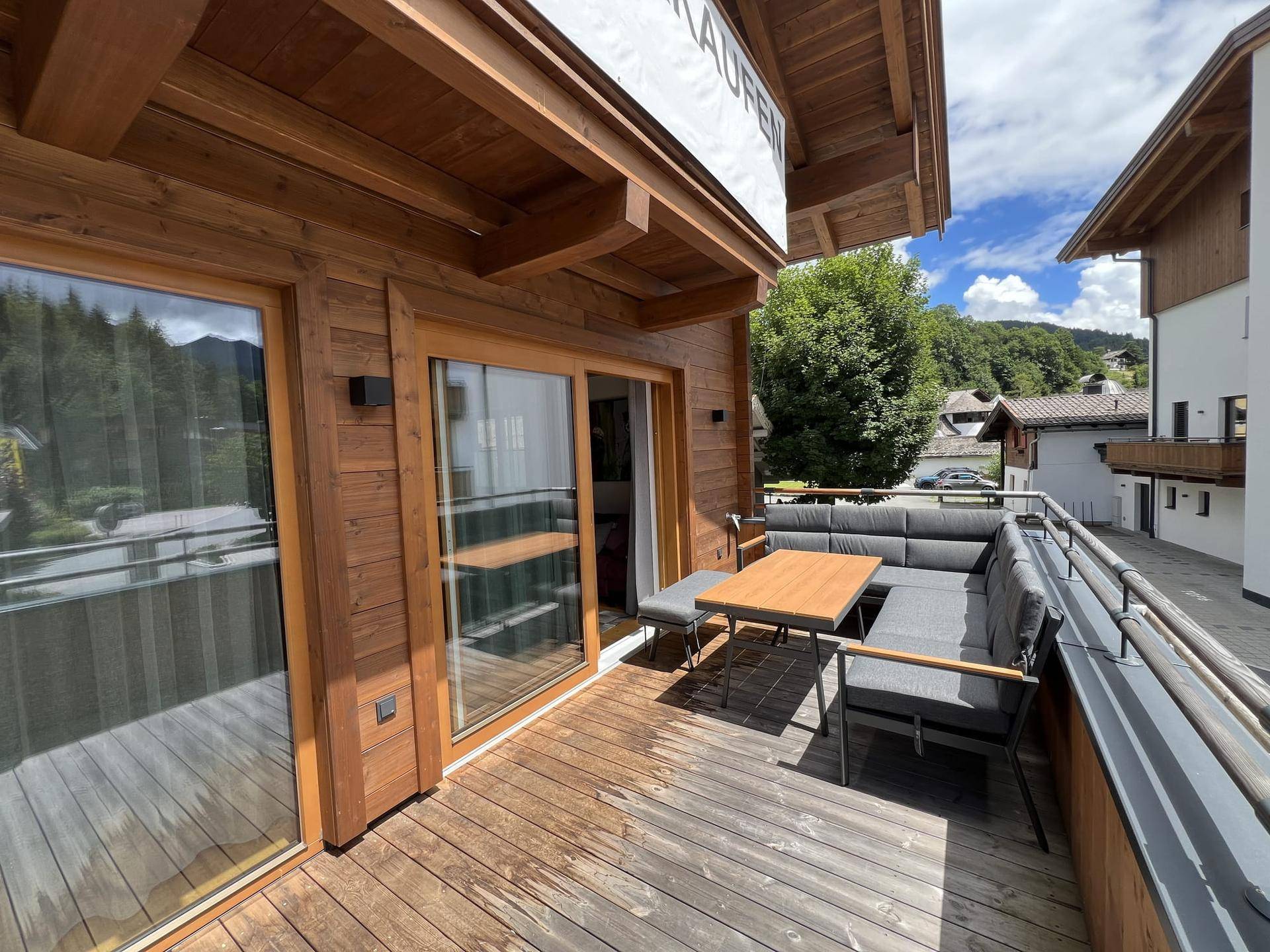 Großer Holzbalkon mit bequemen Outdoor-Möbeln und Blick auf die grüne Umgebung.