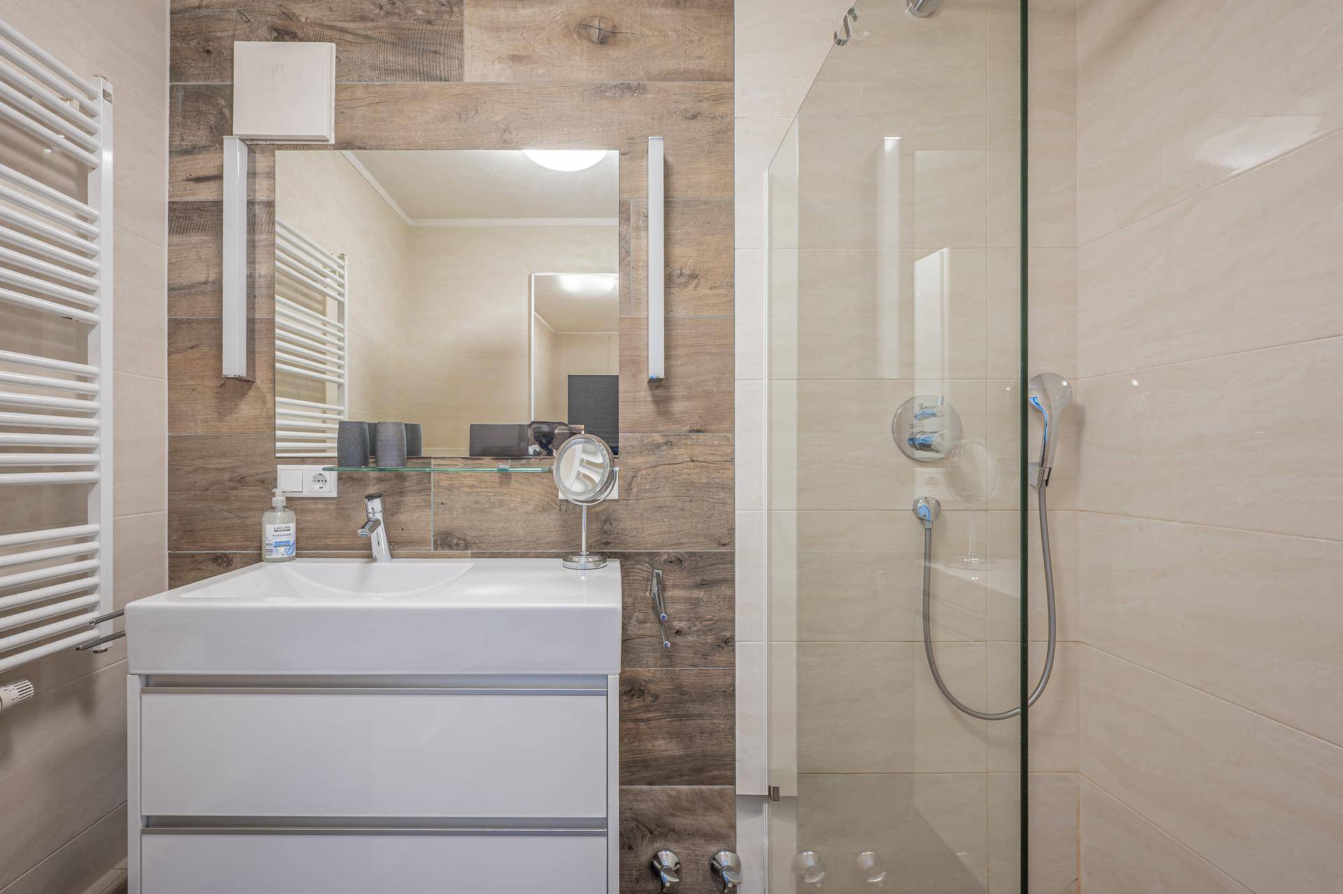 Modernes Badezimmer mit begehbarer Dusche, Einzelwaschbecken und beheiztem Handtuchhalter, hell und funktional.