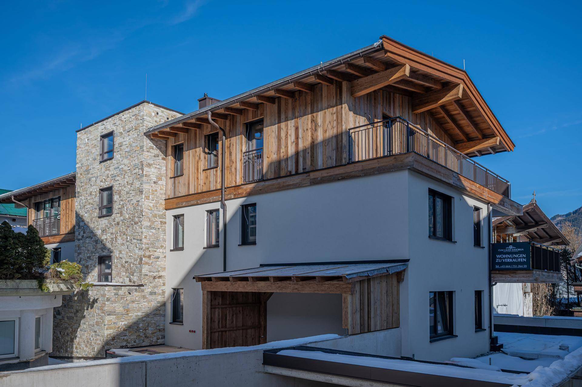 Moderne alpine Architektur des Neubaus mit Holzfassade, Steinelementen und Satteldach.