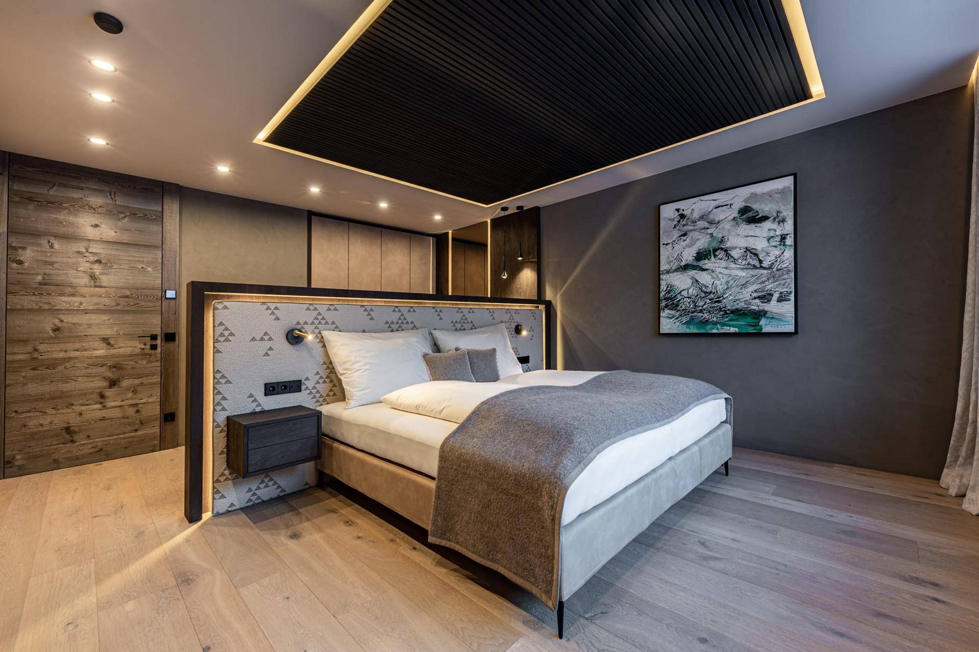 Modernes Schlafzimmer mit Holzboden, dunkler Decke und stilvollem Kopfteil mit integrierter Beleuchtung.