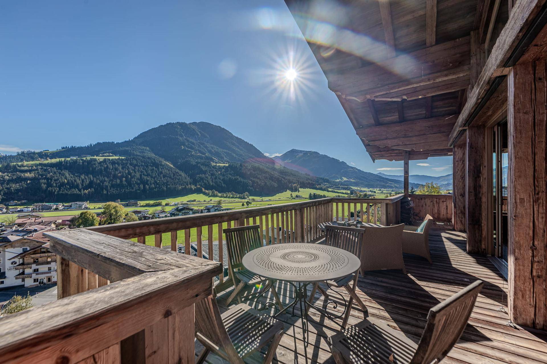 Sonniger Holzbalkon mit Sitzgelegenheiten und weitem Blick auf die umliegende Berglandschaft.