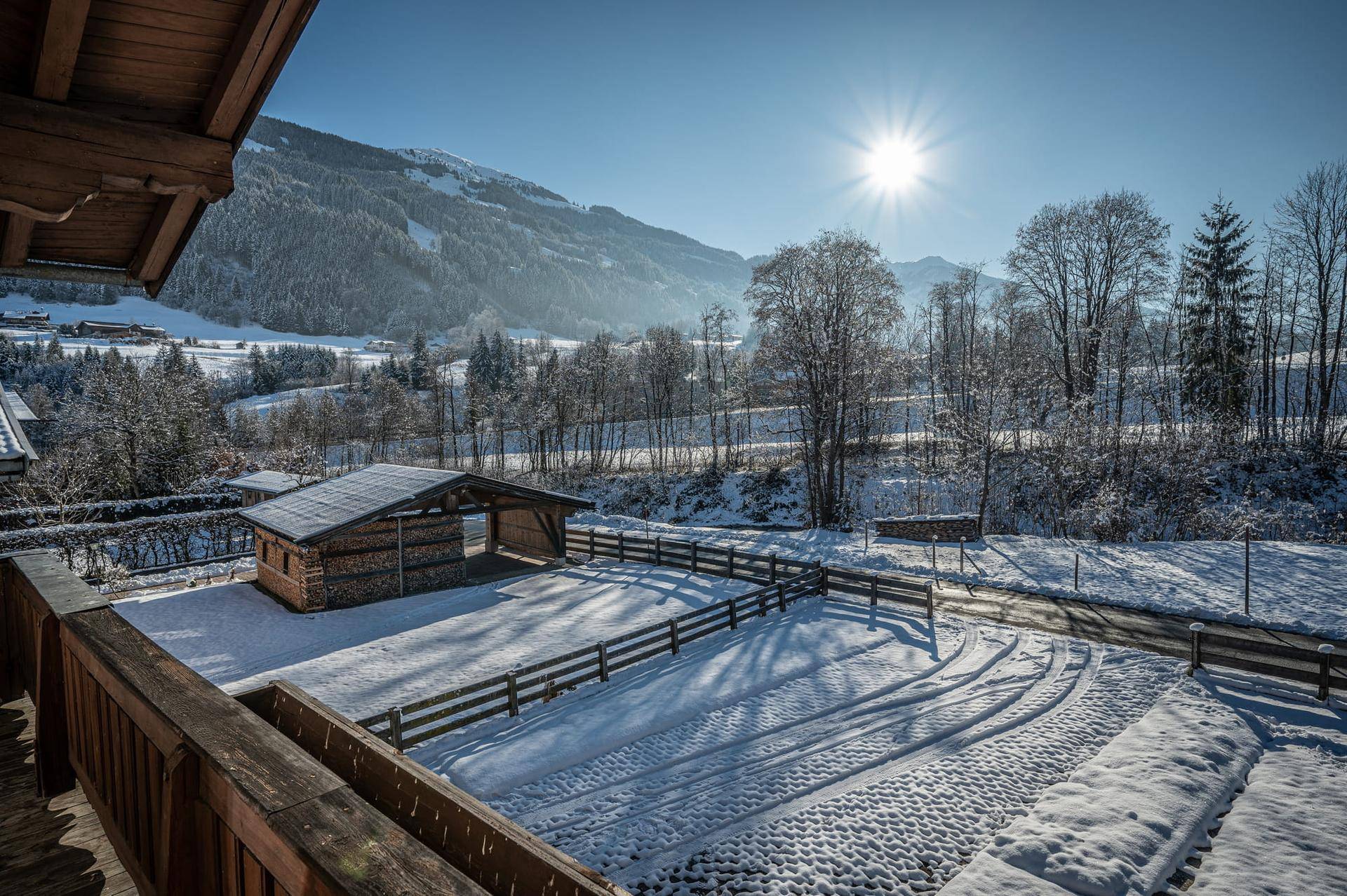 Panoramablick von einem Balkon auf eine verschneite Landschaft mit Holzhütte und Bergen.