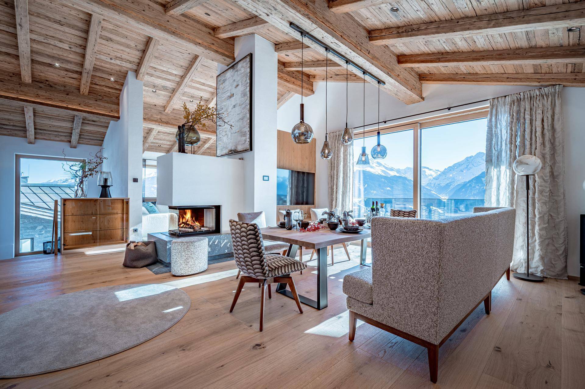 Heller, offener Wohn-Essbereich mit Kamin, Holzbalkendecke und Panoramablick auf die Berge.