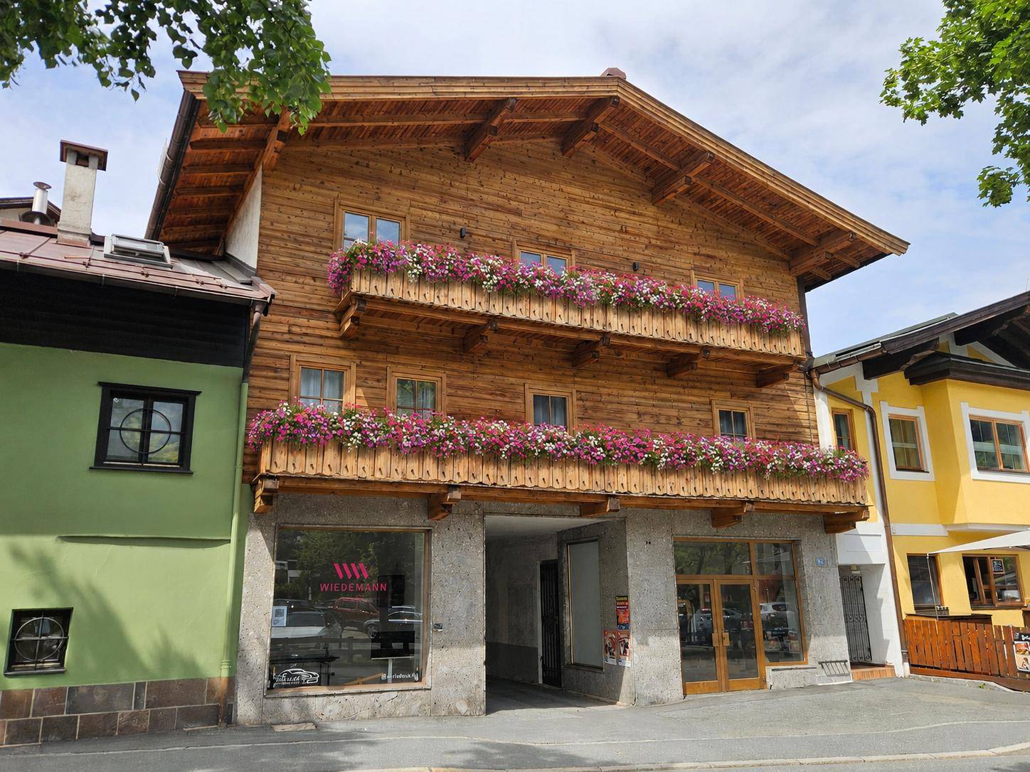 Traditionelles Holzhaus mit blühenden Balkonkästen und Geschäften im Erdgeschoss in alpiner Umgebung.