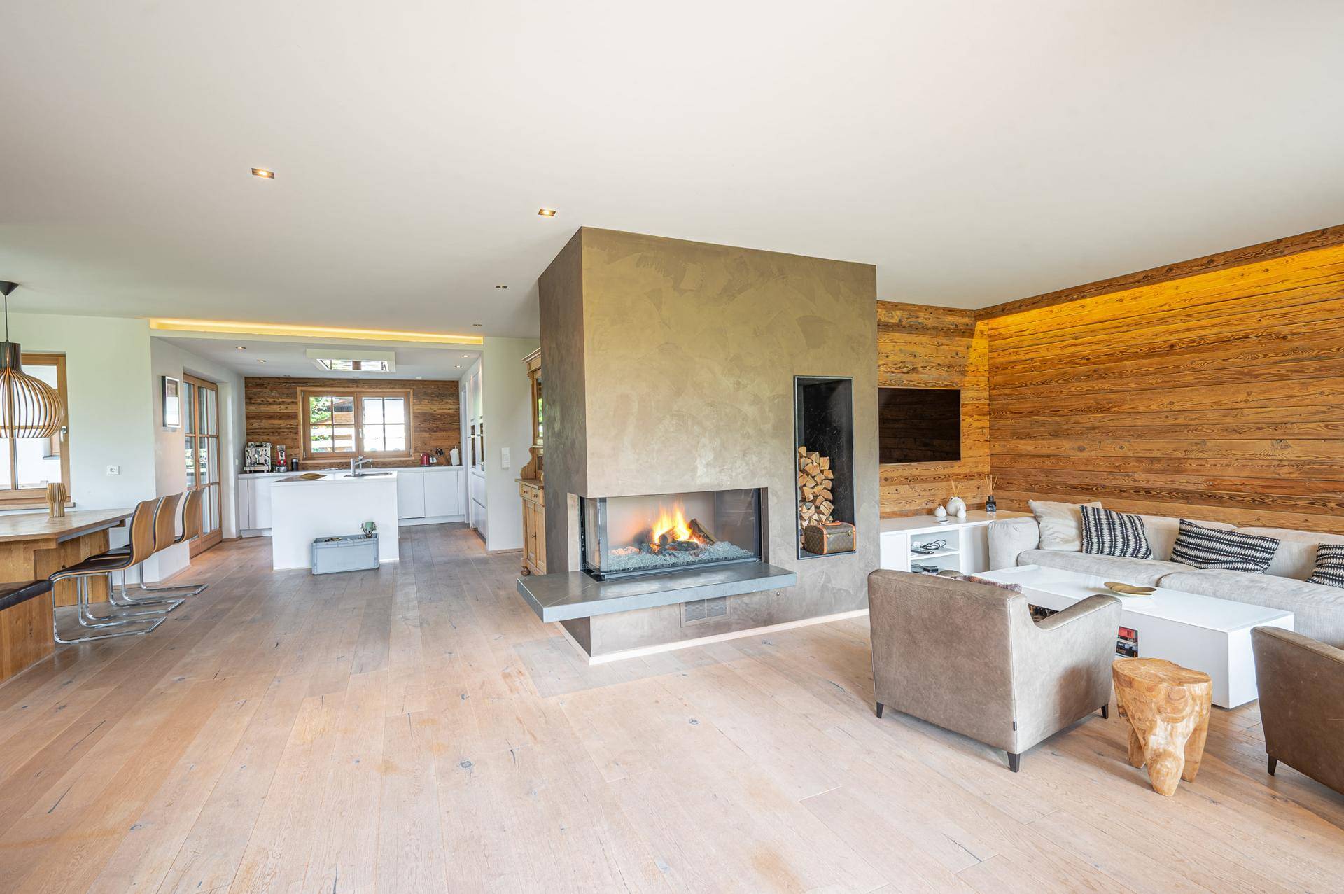 Geräumiger offener Wohnbereich mit modernem Kamin, Holzwänden und Blick auf die Küche.