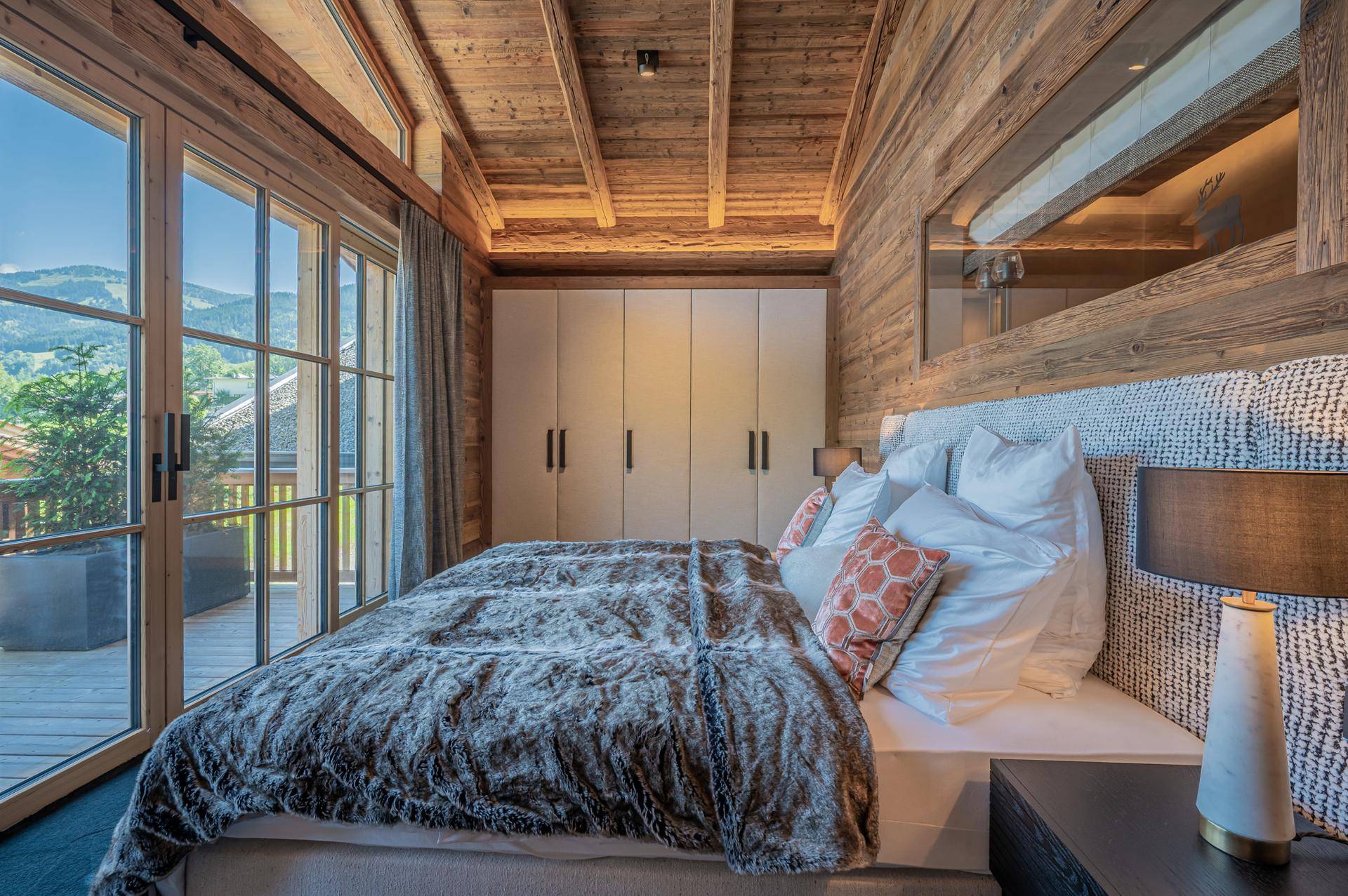 Gemütliches Schlafzimmer mit Holzwänden, Einbauschränken und Zugang zu einem Balkon mit Bergblick.
