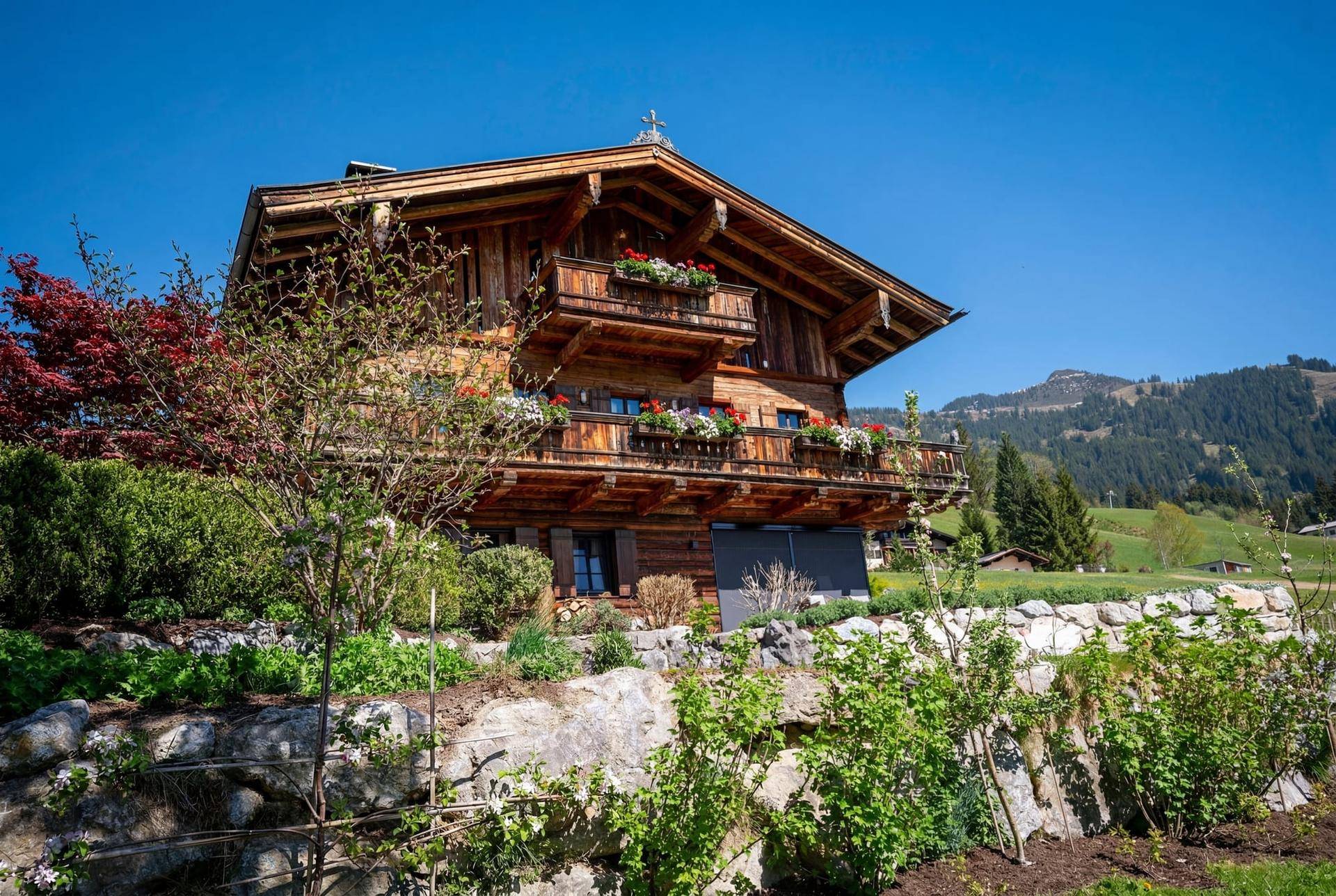 Traditionelles Holzchalet mit blumengeschmückten Balkonen und malerischem Bergblick in grüner Umgebung.