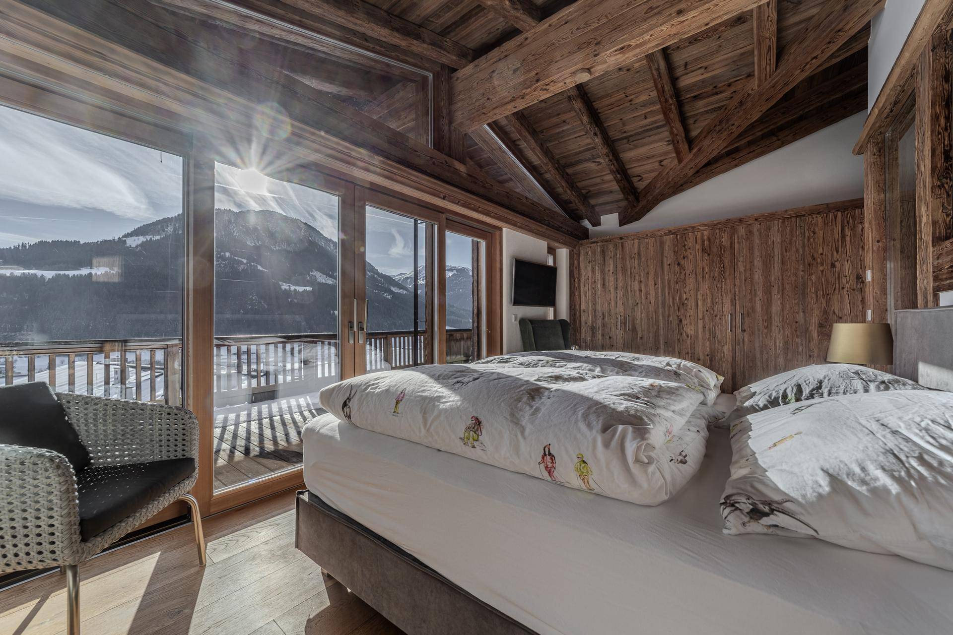 Helles Schlafzimmer mit Holzwänden, großzügigen Fenstern und sonnigem Bergblick.